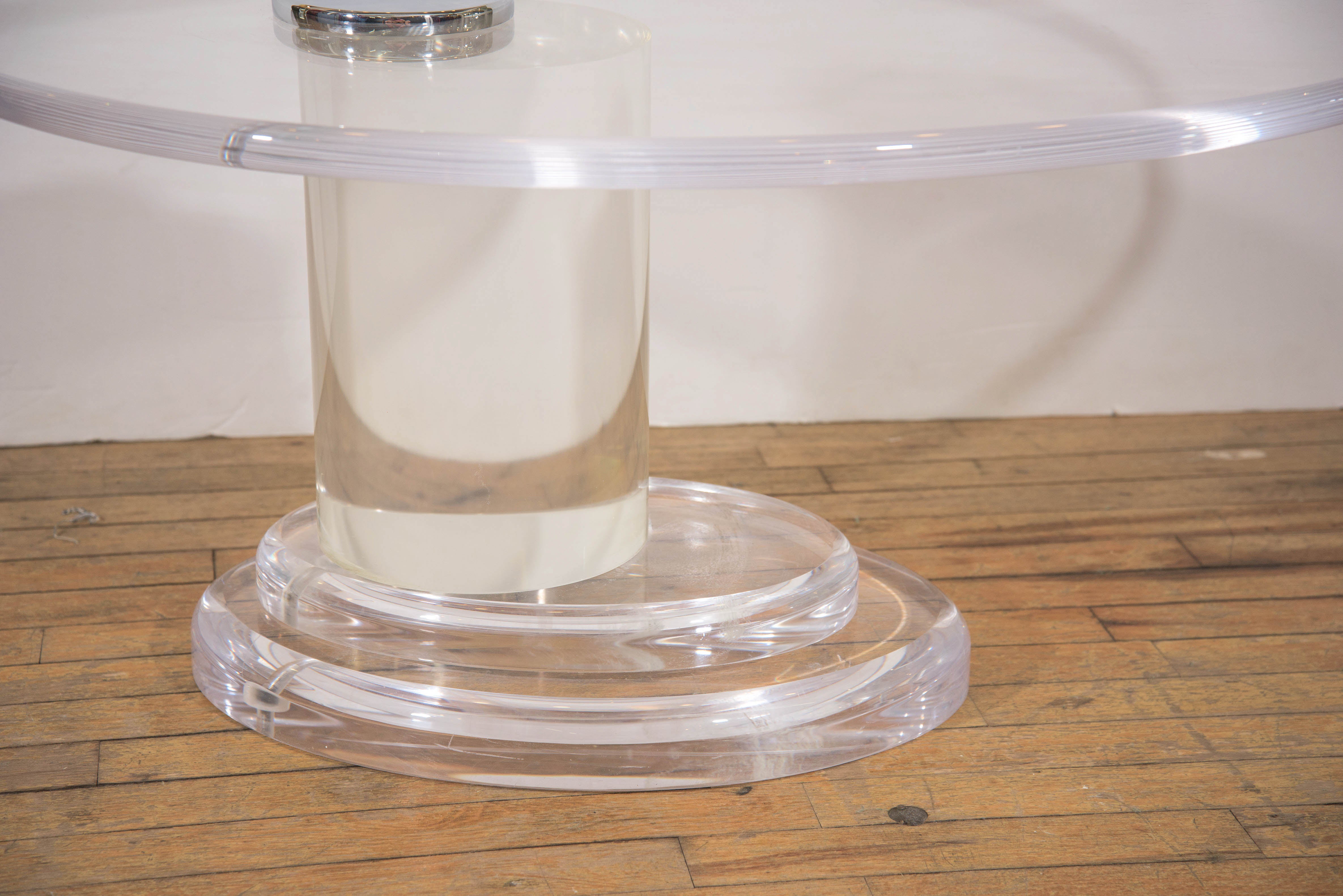 A vintage coffee table, produced circa 1970s by Lion in Frost, in Lucite, with oval top and polished chrome button as accent, above a thick column on a two-tier, stepped oval base; tabletop swivels, for adjustment. Good vintage condition, consistent
