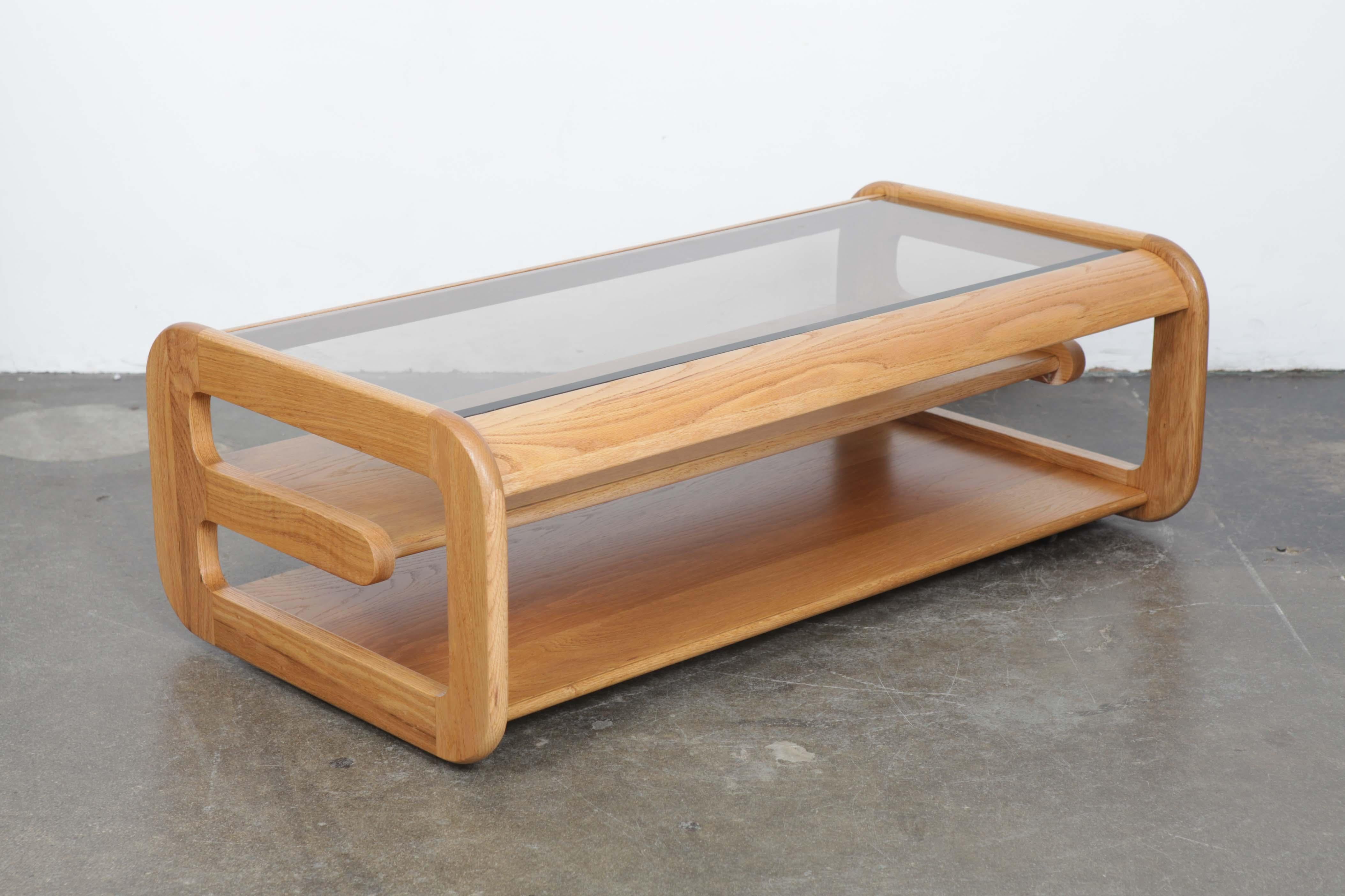 Newly refinished oak and smoke glass top coffee table designed by Lou Hodges for California Design Group, 1970s, with cantilevered centre shelf and upper glass top inset into the oak frame. Glass is original and has scratches commensurate with wear.