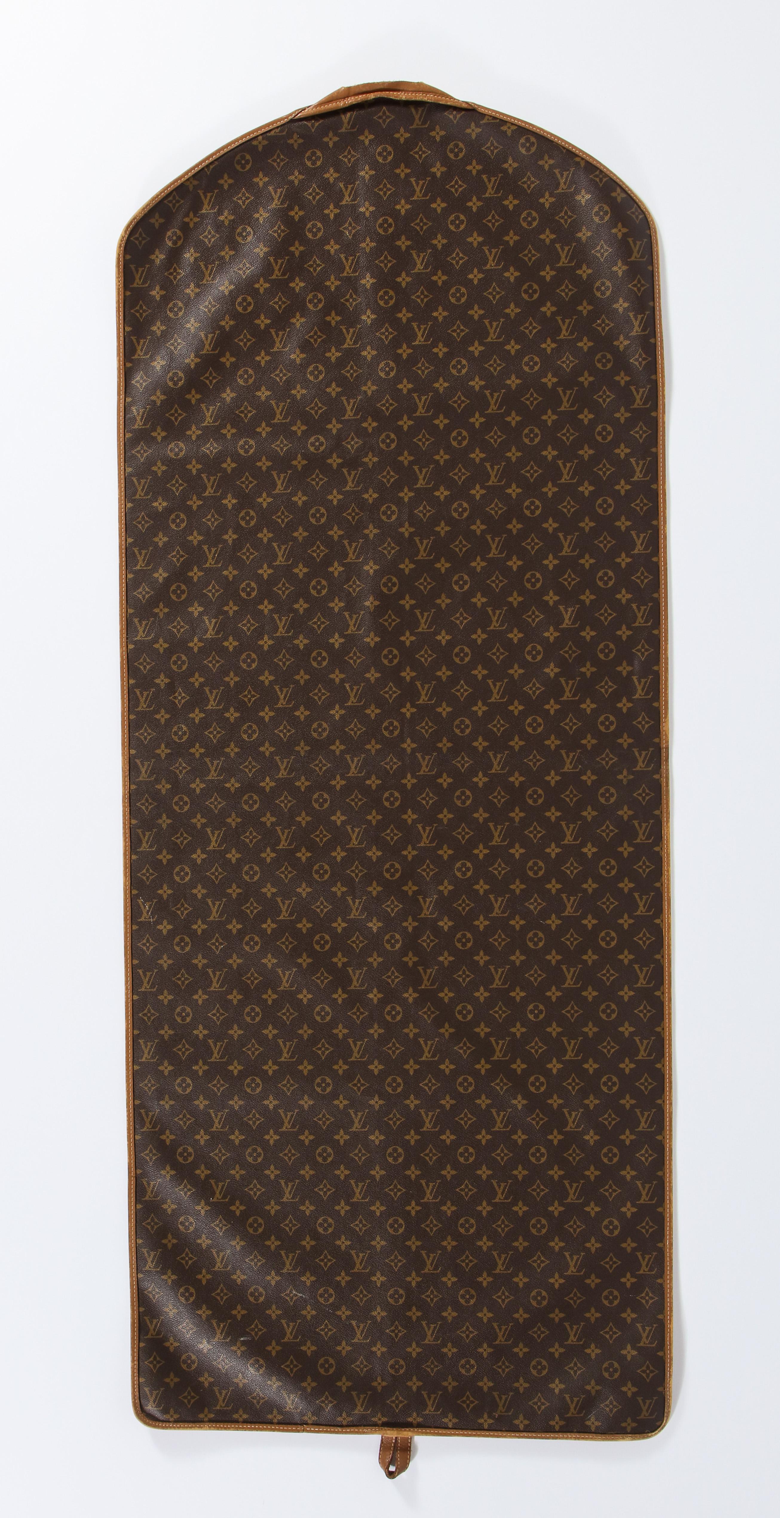 Slim Louis Vuitton monogram garment cover in brown coated canvas with leather trim. Made by The French Company in the 1970s. Open hanger slit at the top with a leather loop at the bottom; some rubbing wear around the trim particularly at the top.