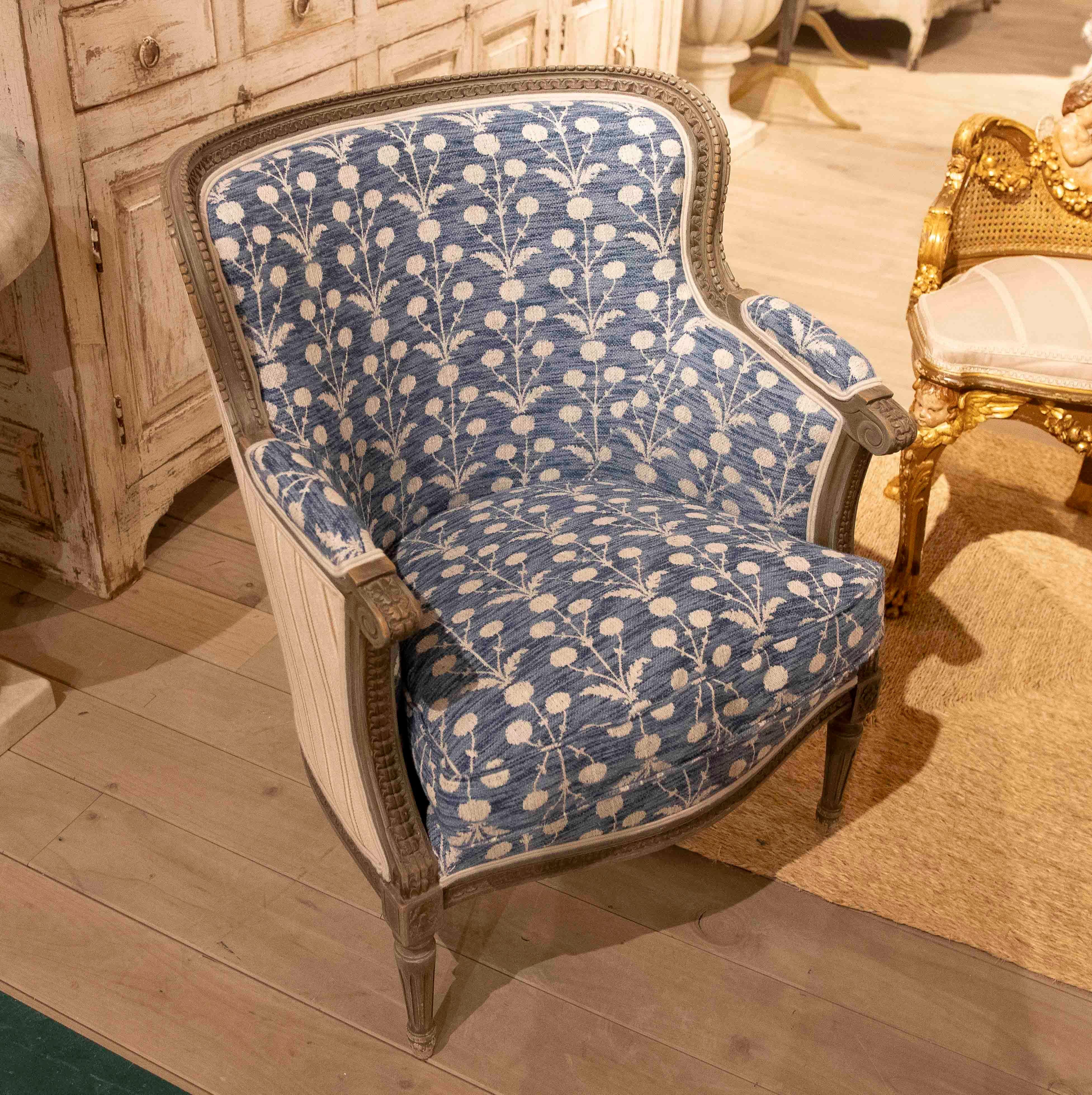 Elegant Louis XVI-inspired armchair with a carved wooden frame finished in an antique grayish tone. The upholstery stands out for its original indigo blue linen fabric with a white floral pattern, lending a fresh and personal touch to the piece.
The