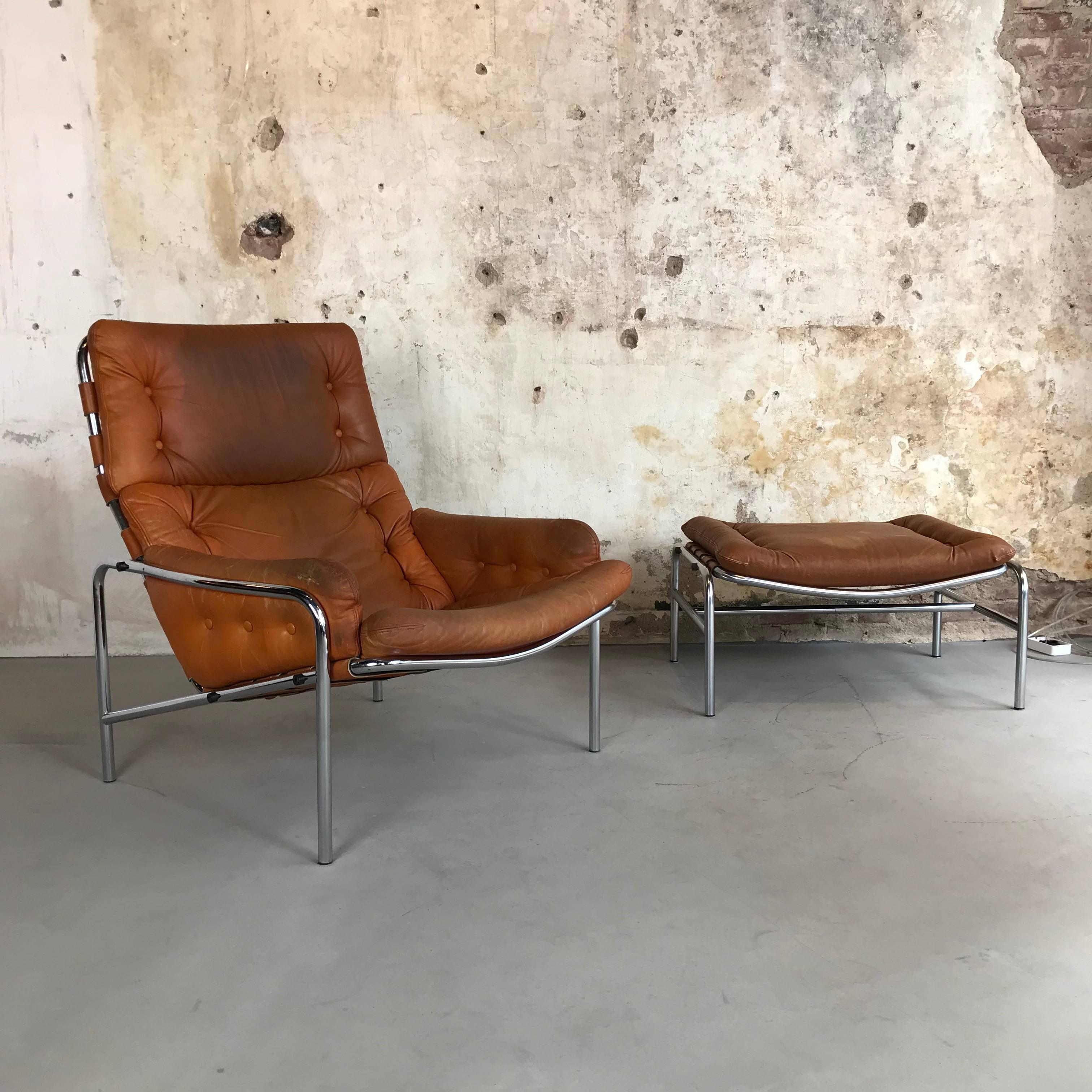 This armchair and ottoman still features the original cognac/camel leather upholstery and wears a beautiful aged patina. The right arm of the chair has a small handrail restoration scar what gives the chair even more character. Chrome is still very