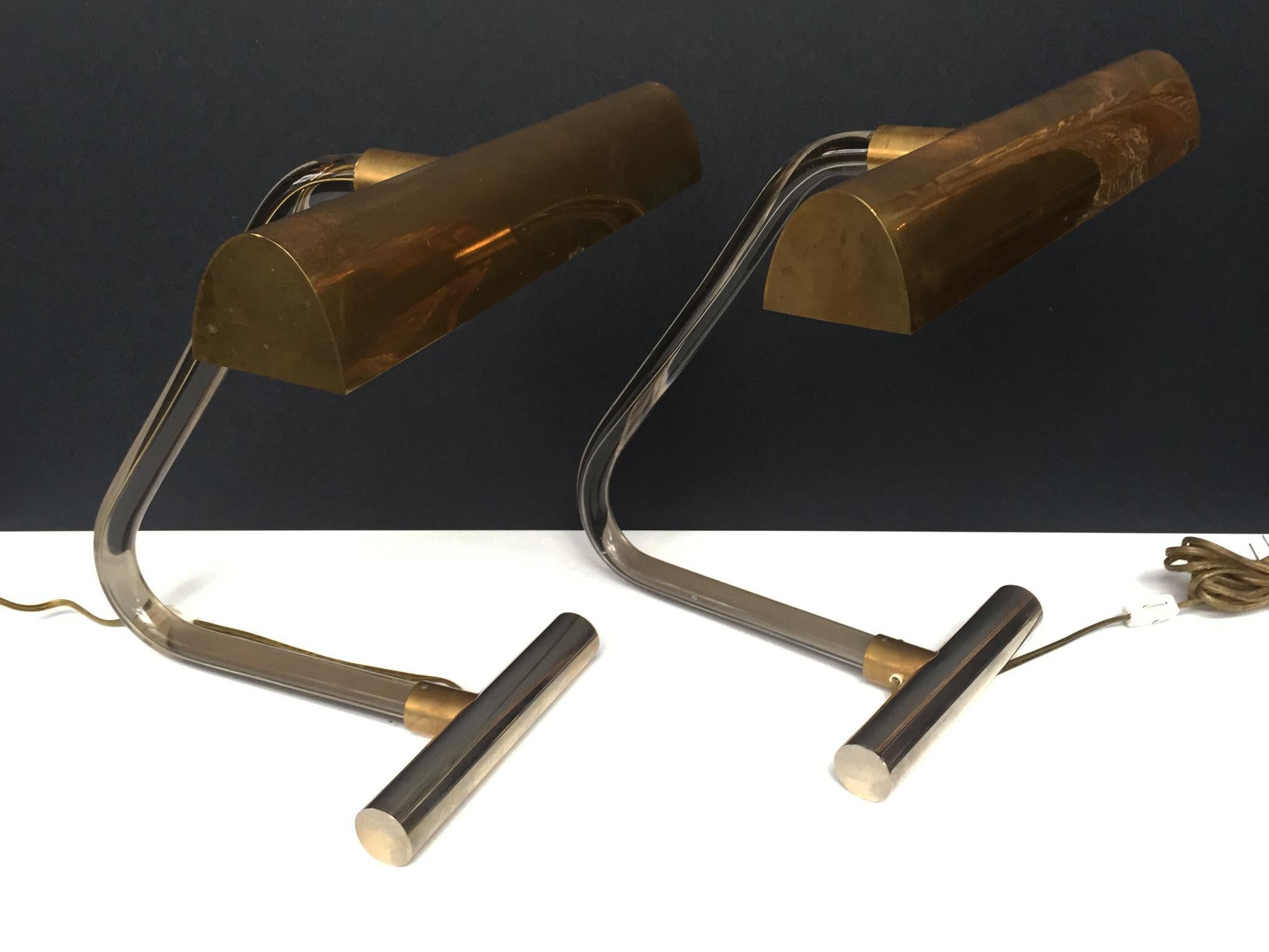 These 1970s luxe desk lamps were designed by Peter Hamburger and manufactured by George Kovacs as part of the Crylicord collection. They are comprised of smoked Lucite stems, brass shades, and chrome counterweight bases. With their balance of smooth