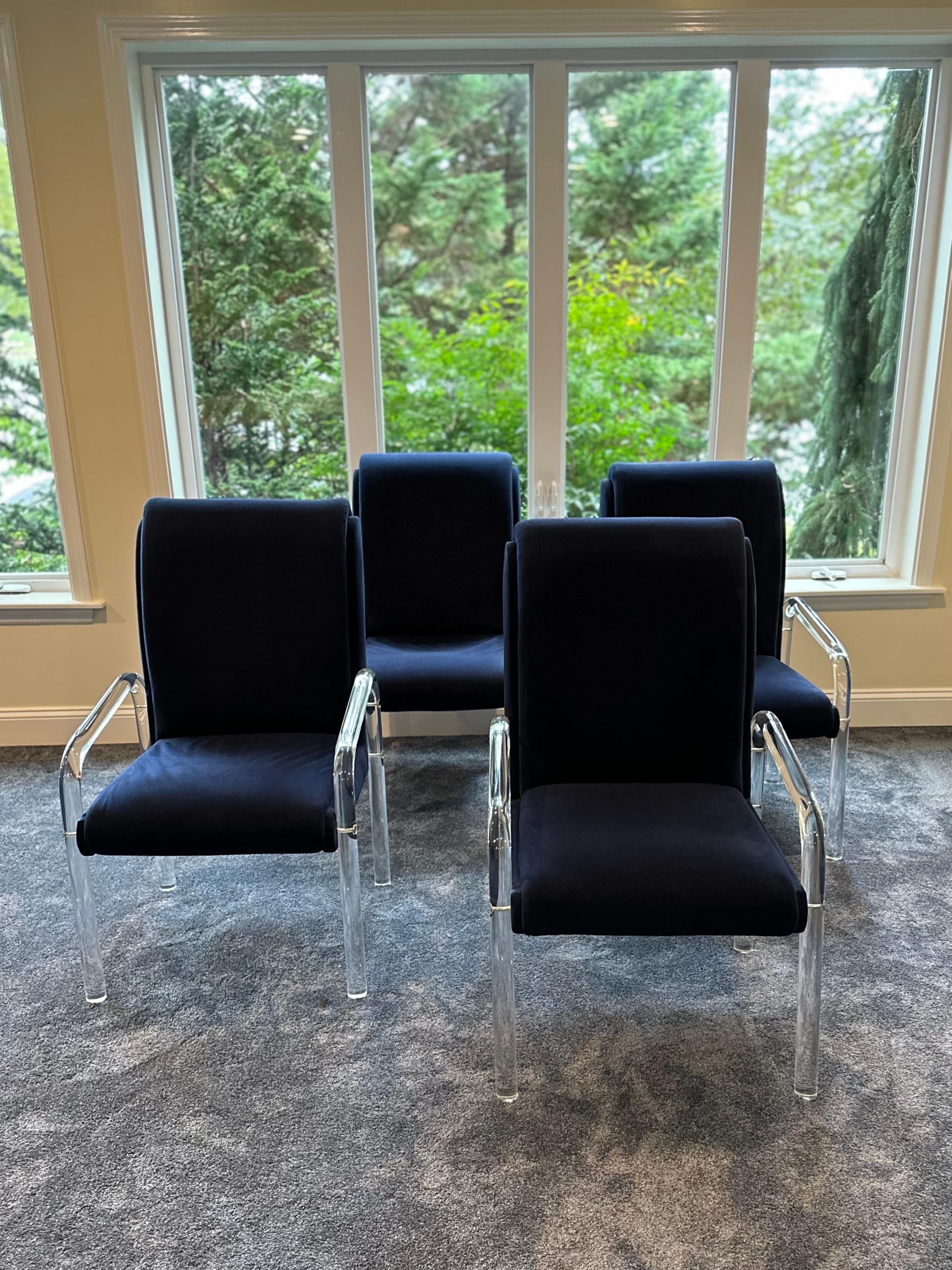 Un bellissimo set di quattro lussuose sedie da pranzo con telaio in lucite curvato e dettagli in ottone. Le sedie sono rivestite con il tessuto originale blu navy che mostra una certa usura dovuta all'età e all'uso; una nuova tappezzeria le