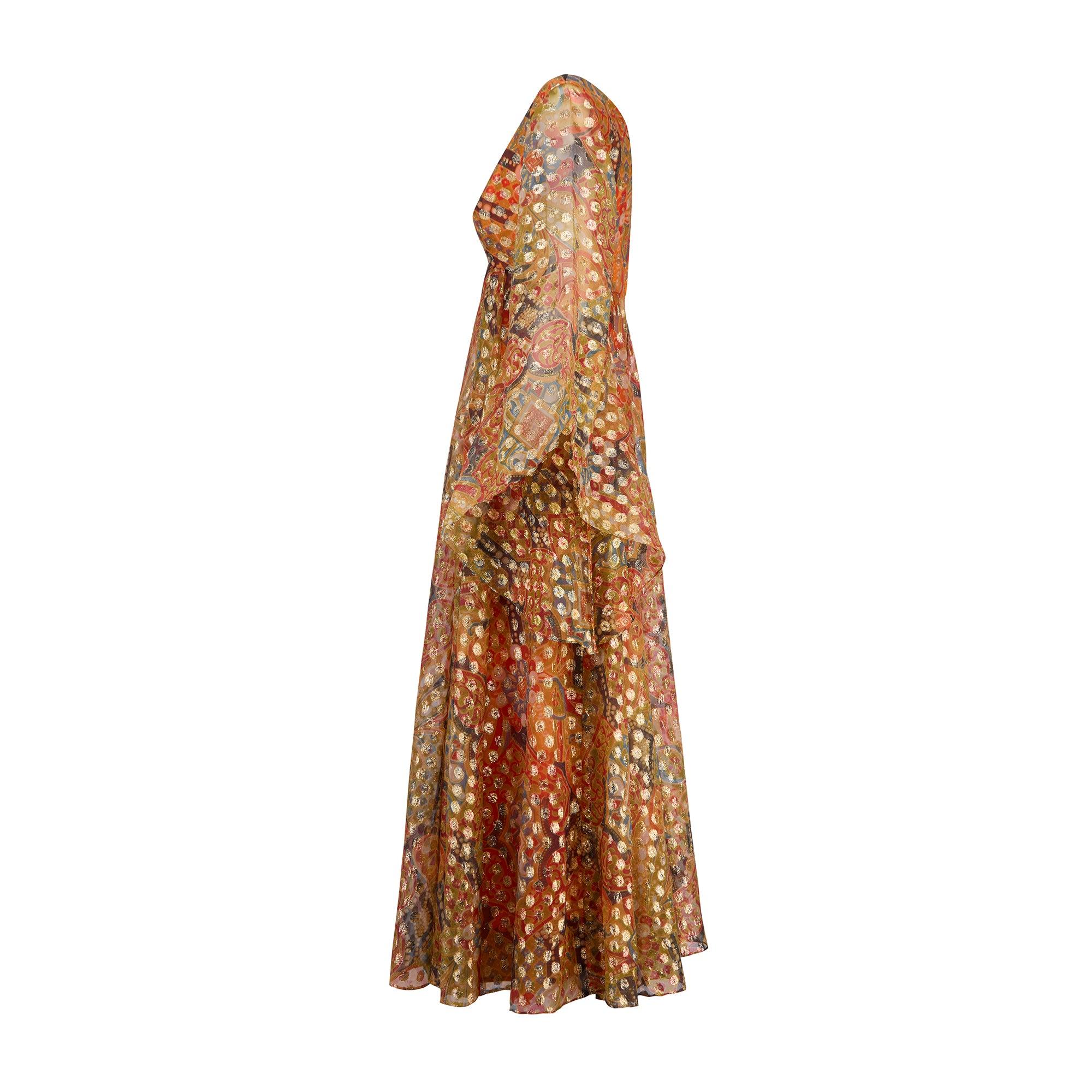 Cette remarquable robe longue a été conçue par Madelyn Modes pour Fredericks Freeport entre la fin des années 1960 et le début des années 1970.  Le tissu est envoûtant : une mousseline de soie raidie de couleur mandarine, imprimée d'un motif
