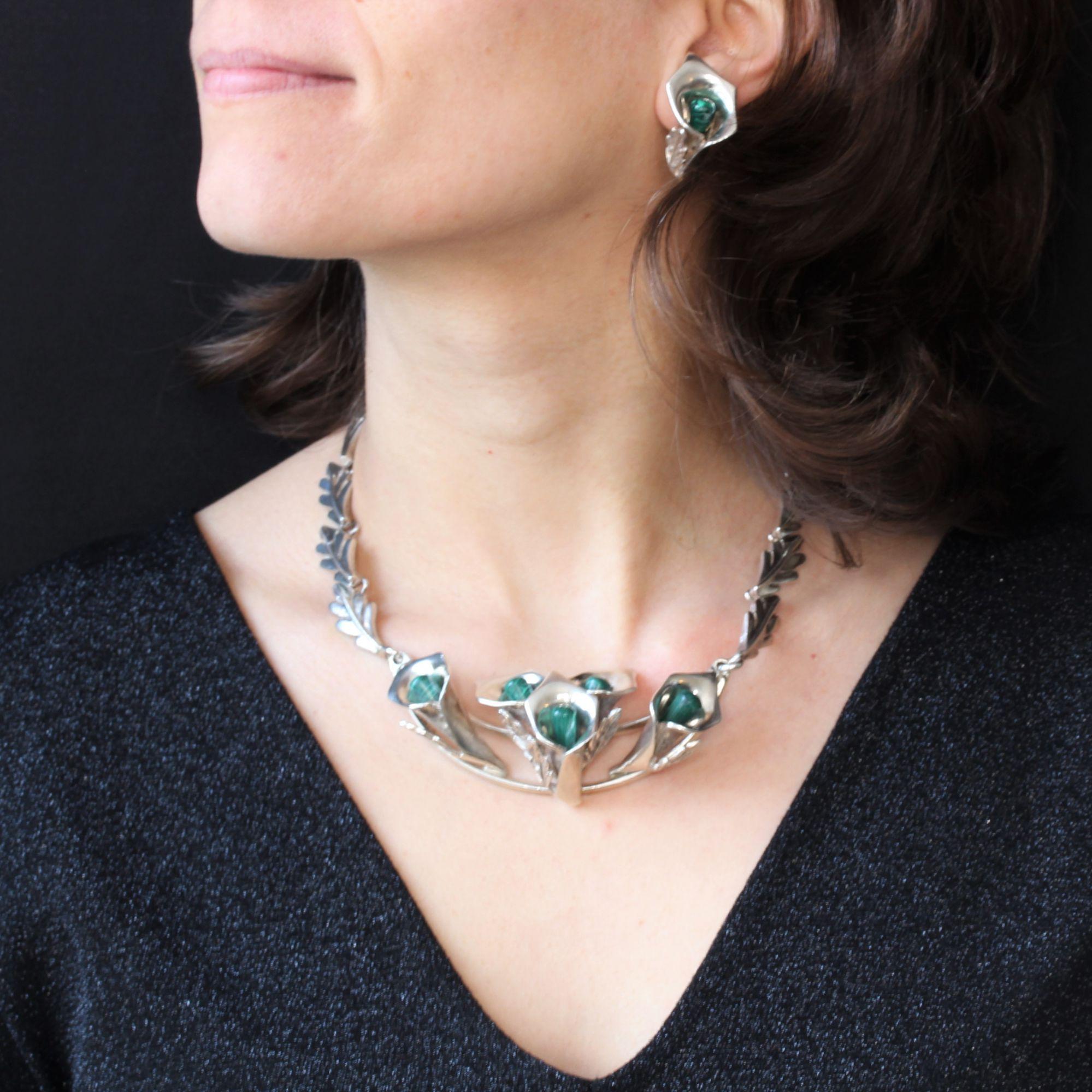 Set in sterling silver, consisting of a pair of clip-on earrings and a large necklace.
This retro silver set is made of arum flower motifs whose heart is a malachite stick. Large silver leaves hold the central motif of the necklace and dress each