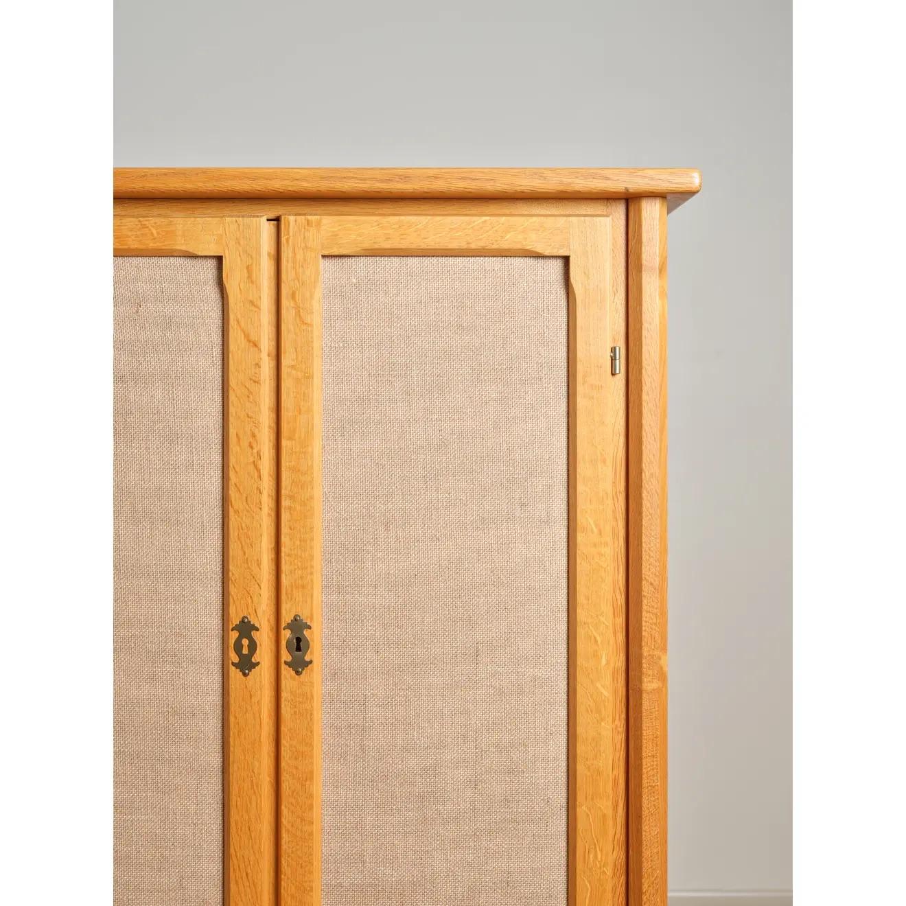 Scandinavian Modern petite armoire in quarter-sawn oak, with burlap-wrapped recessed panel doors and incised motifs at the drawer fronts. In the manner of Henning (Henry) Kjaernulf, c. 1970's. Key included.