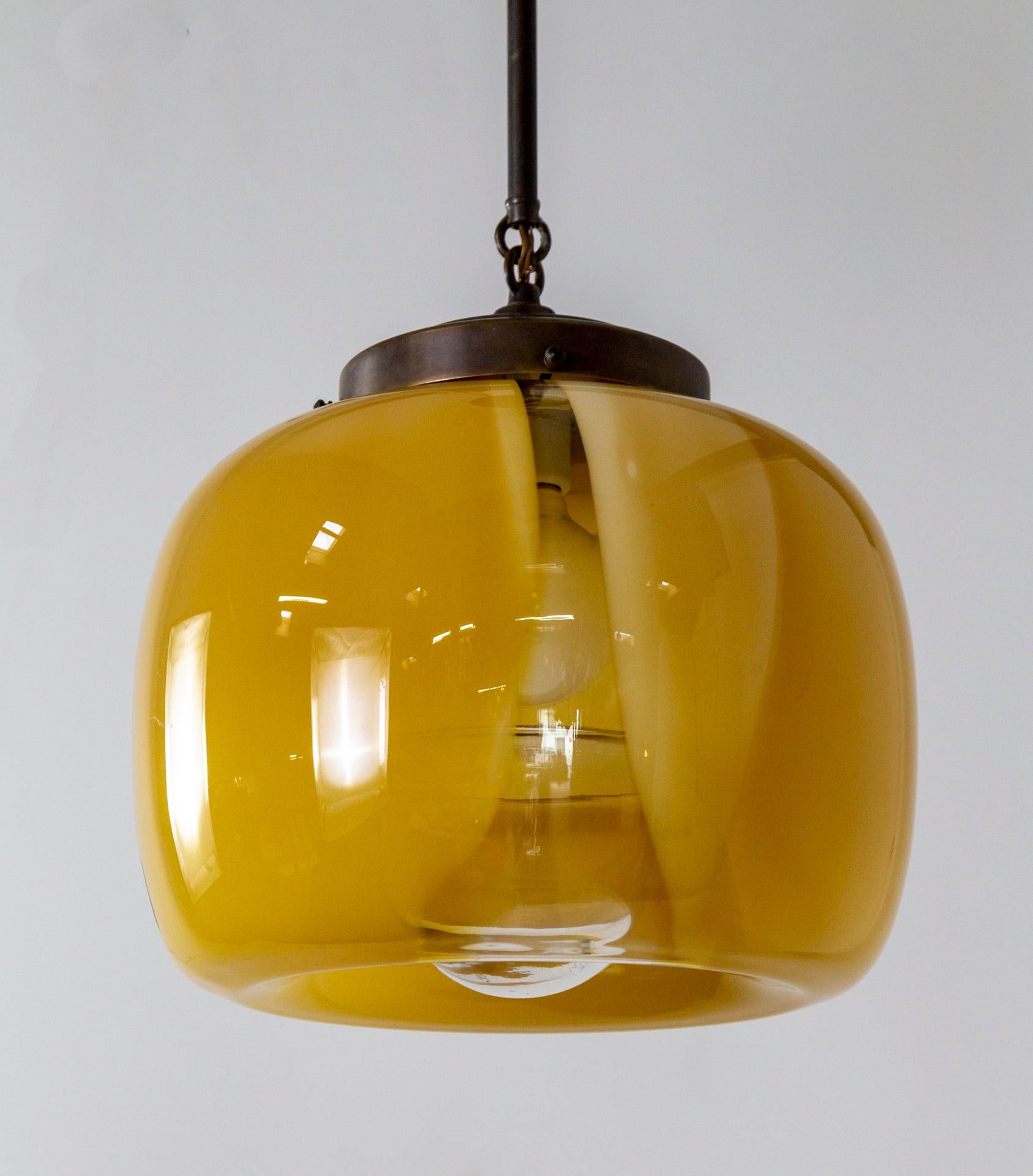 Une lampe suspendue avec un abat-jour complexe en verre de Murano, soufflé à la main, de couleur jaune ambré laiteux avec une strie claire qui révèle l'intérieur.  Le baldaquin, la tige et le support de l'abat-jour sont en laiton de couleur bronze. 