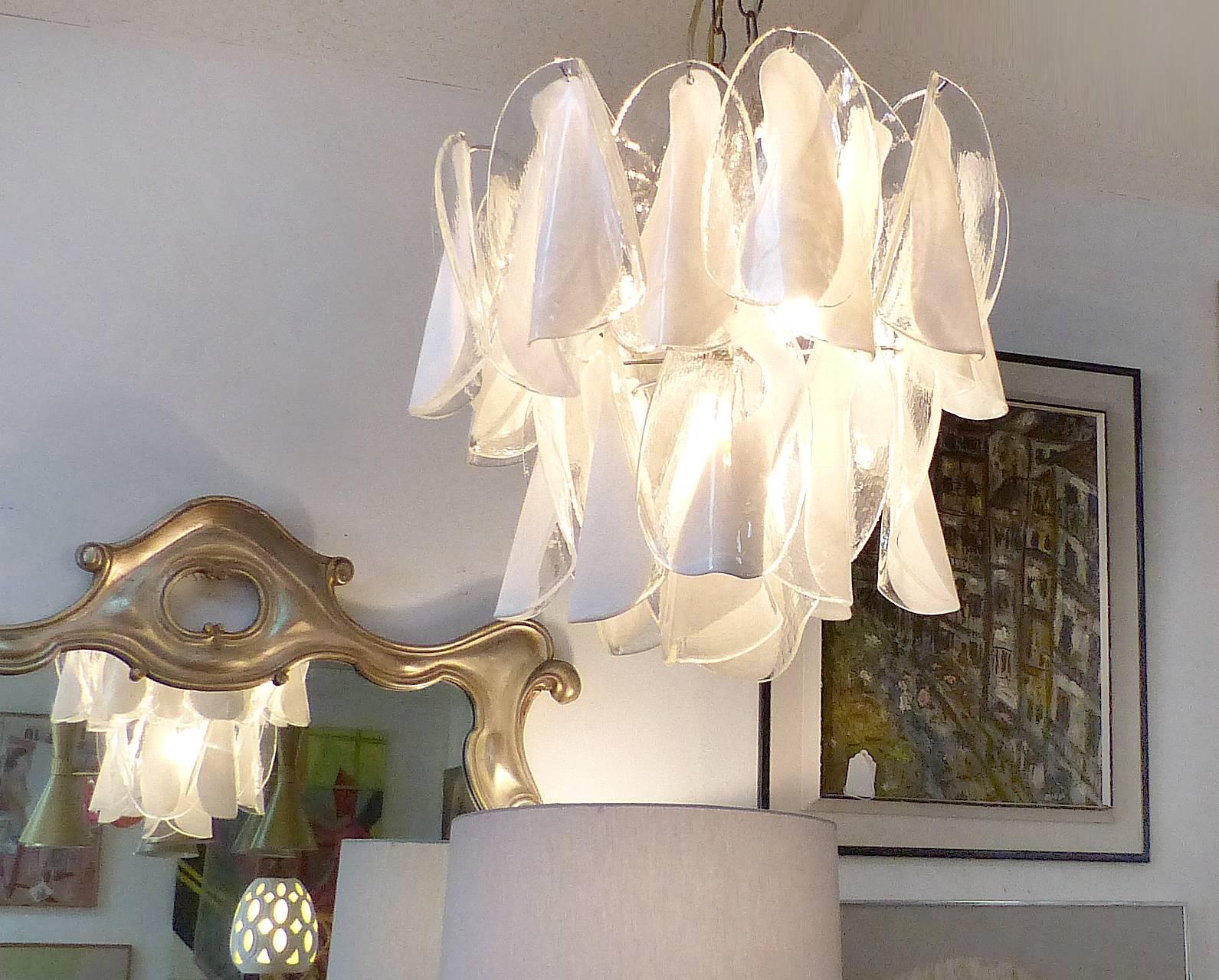 Offered for sale is a Mazzega Murano chandelier created with elegant handblown clear and white petals design, The two-tier Italian 1970s fixture has three standard chandelier bulbs above and a fourth which aims downward. The measurements given are