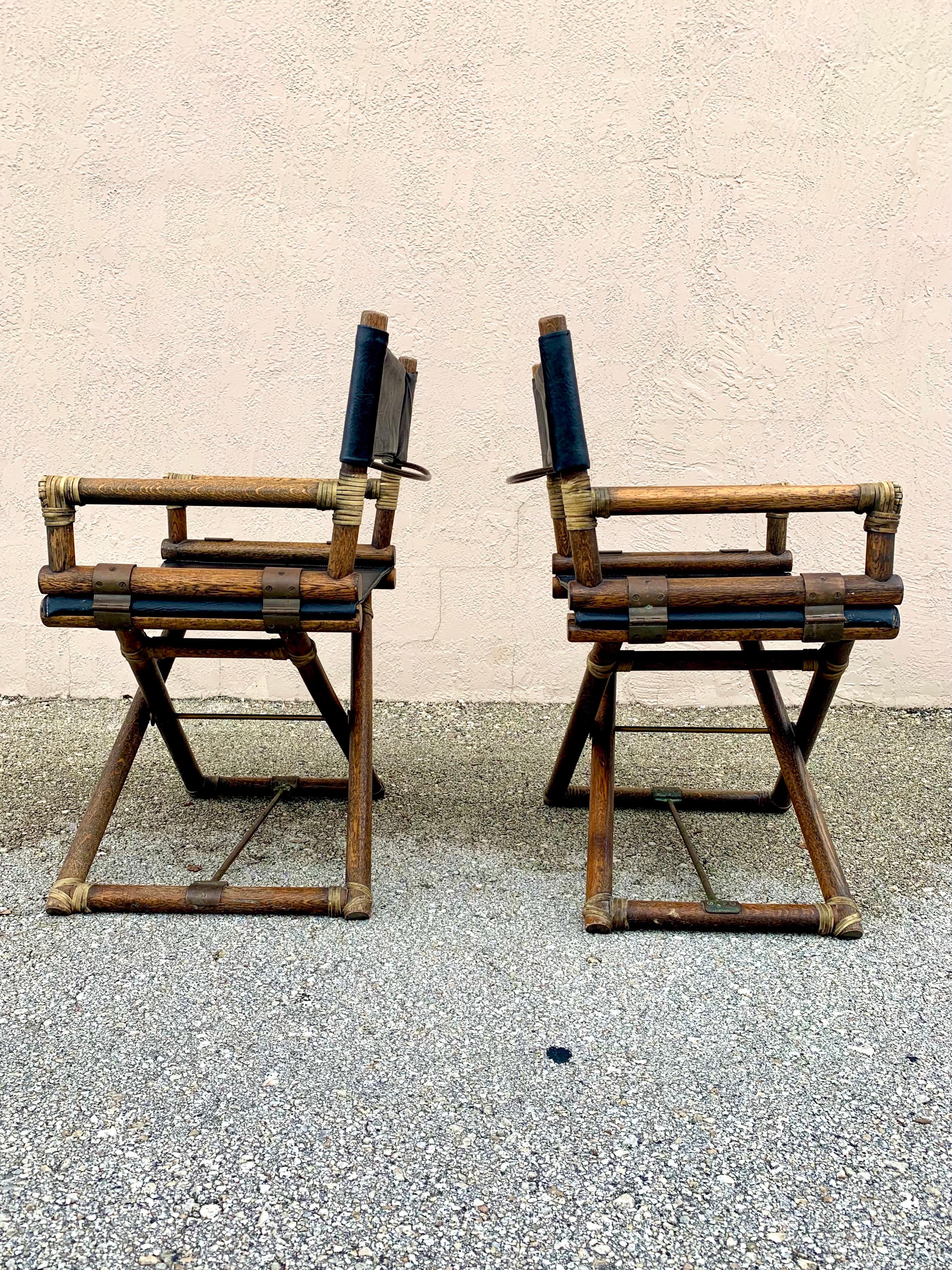Stunning pair of director chairs made by McGuire Furniture. Oak affixed with rawhide leather wrapping, brass hardware, and high quality black vinyl. All original with incredible patina on the oak and brass. Chairs do fold down for easy storage when