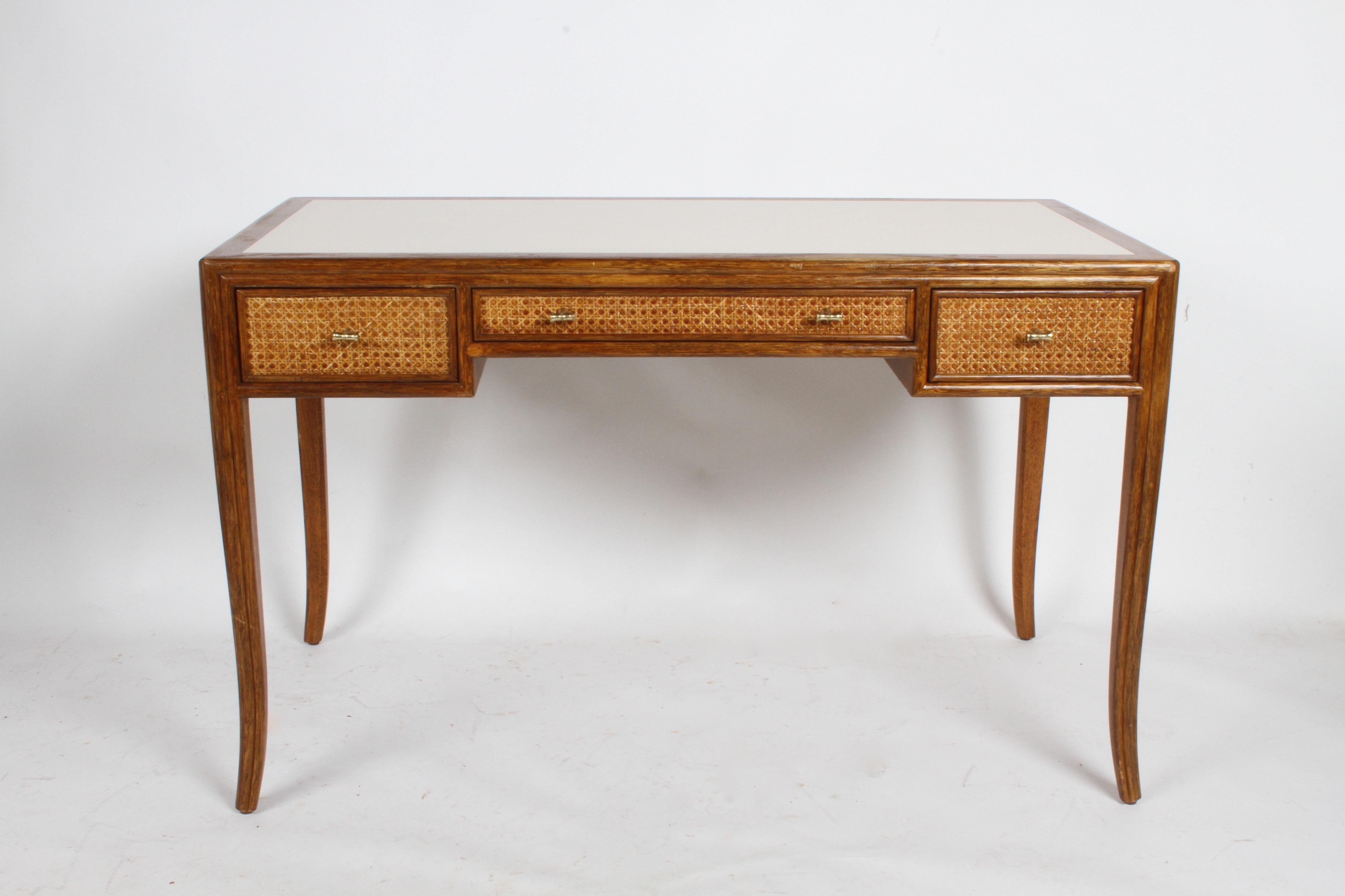 1970s McGuire furniture of San Francisco designed desk with splayed legs, caned panels and faux brass pulls. This elegant design, reminds me of T.H. Robsjohn-Gibbings designs for Widdicomb and Baker. Rattan frame with crème laminate top, frame to be