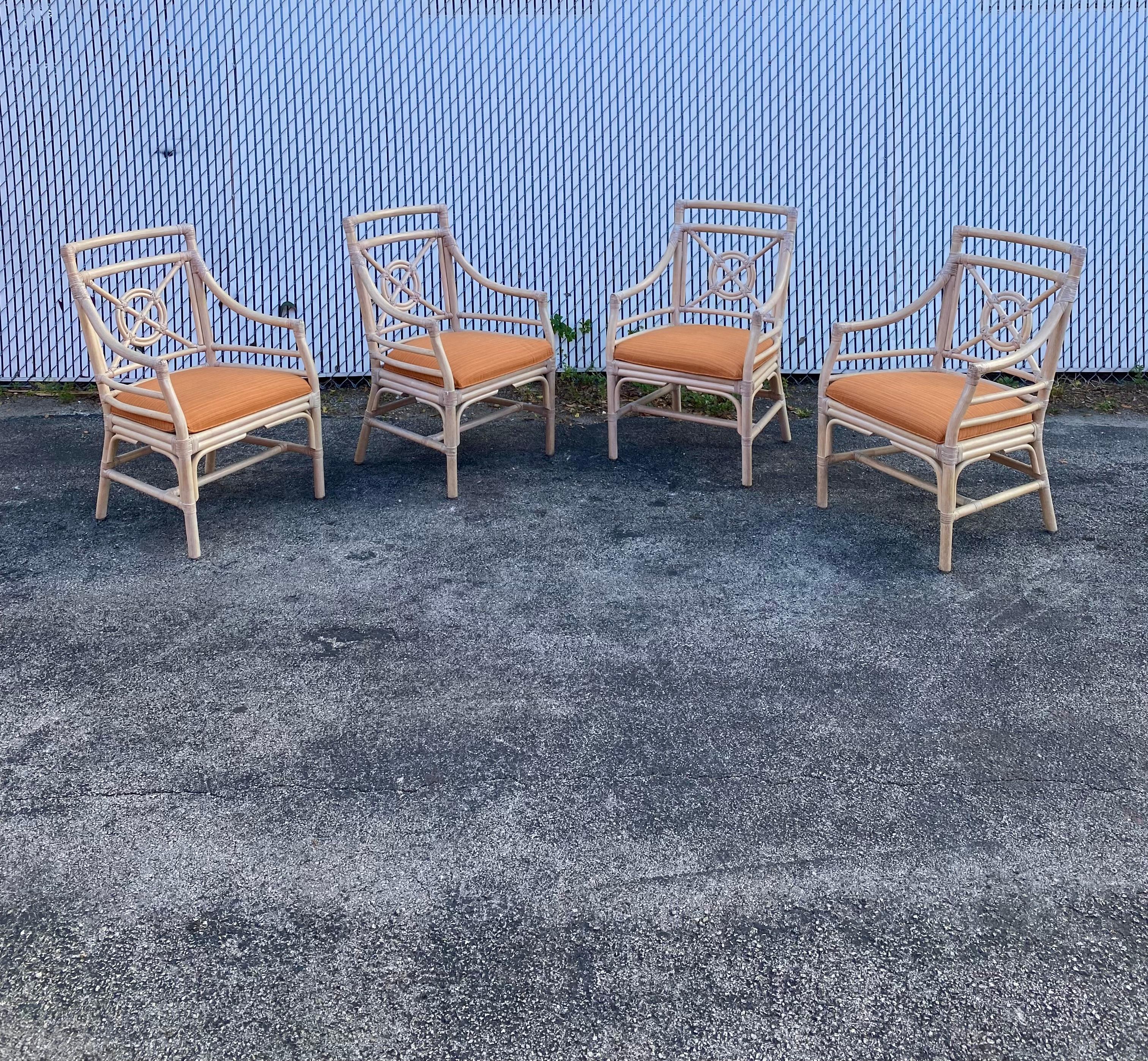 Handsome set of four rattan dining armchairs crafted in the manner and style of McGuire. They feature a bullseye target design on the square back splat. Graceful arms conjoin to a generous seat with orange upholstery. Arms measure 25 inches high.