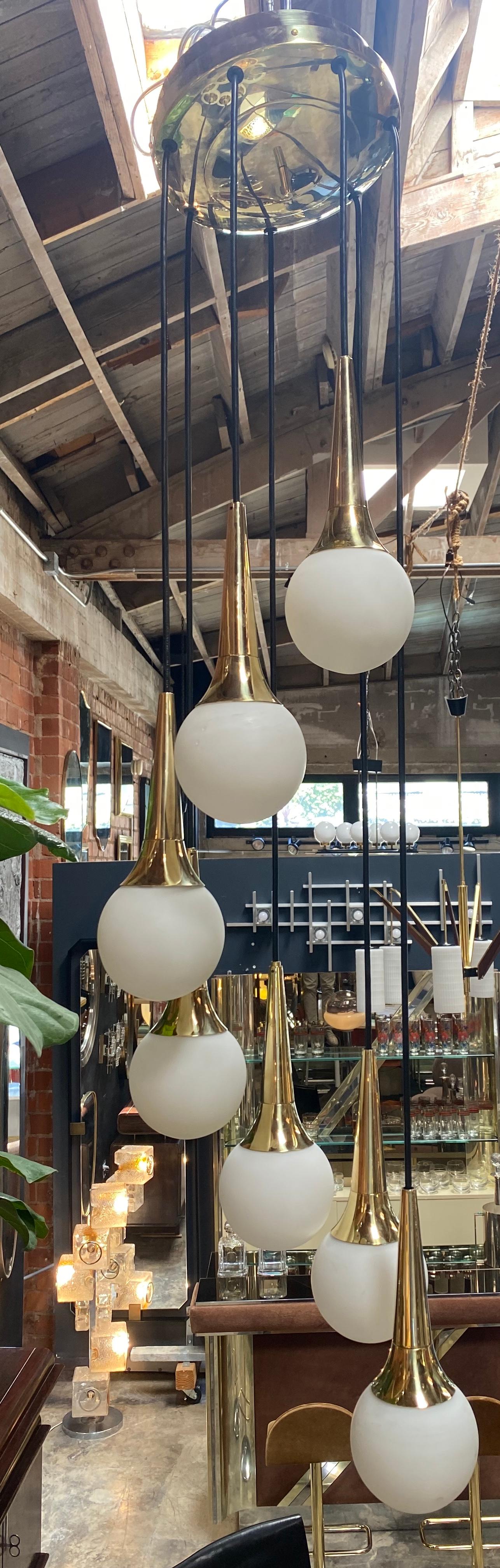 Mid-Century Modern cascading chandelier attributed to Stilnovo with seven opaline glass ball lights supported by brass canopies and suspended by adjustable black plastic wiring. The glass lighting can be adjusted via the plastic wiring to various