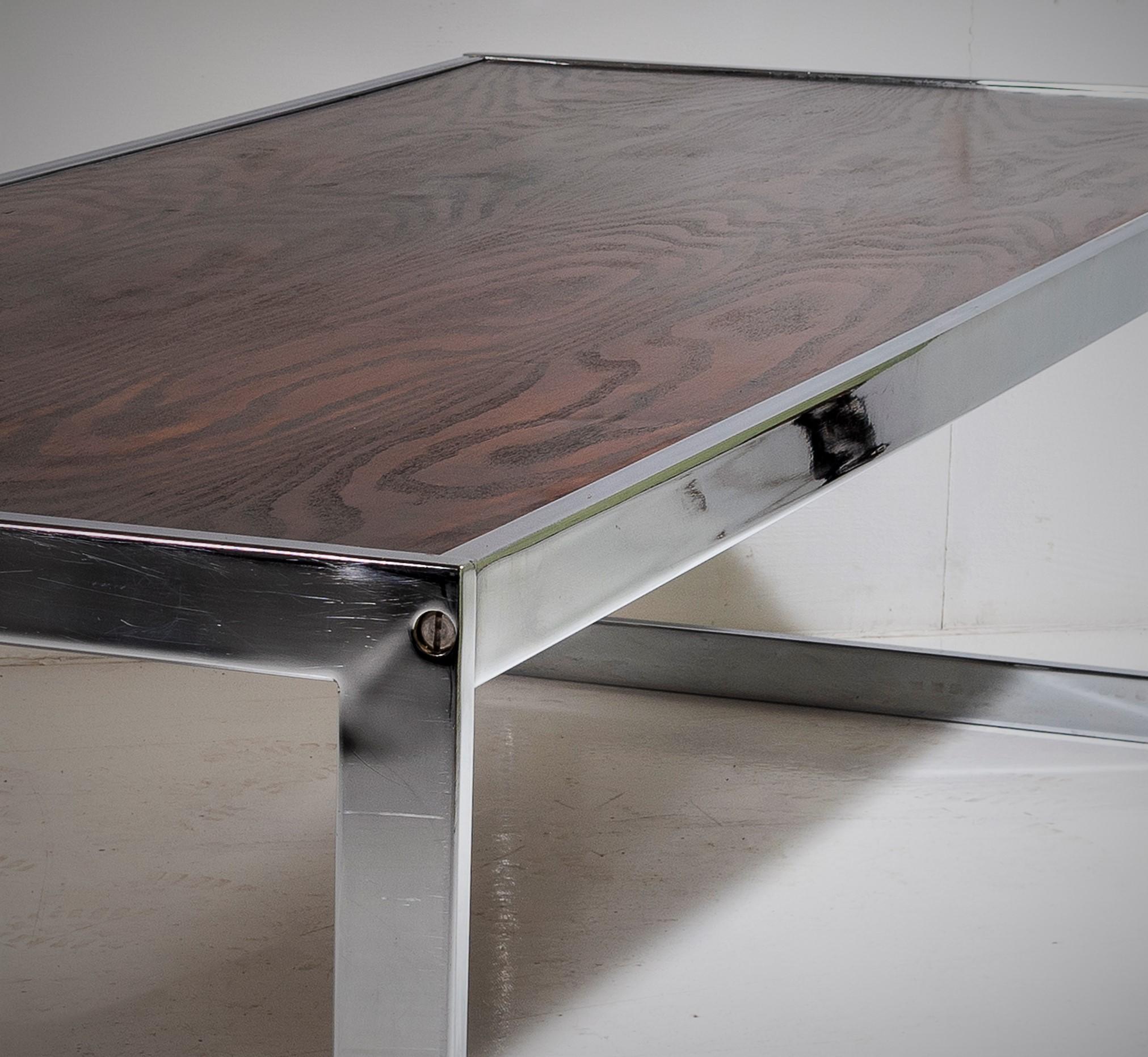 A large mid century coffee table on a chrome base in the manner of Merrow Associates in excellent condition  The top has a superb wood grain veneer to it and has a dark rosewood finish which provides a stylish contract against the bright chrome