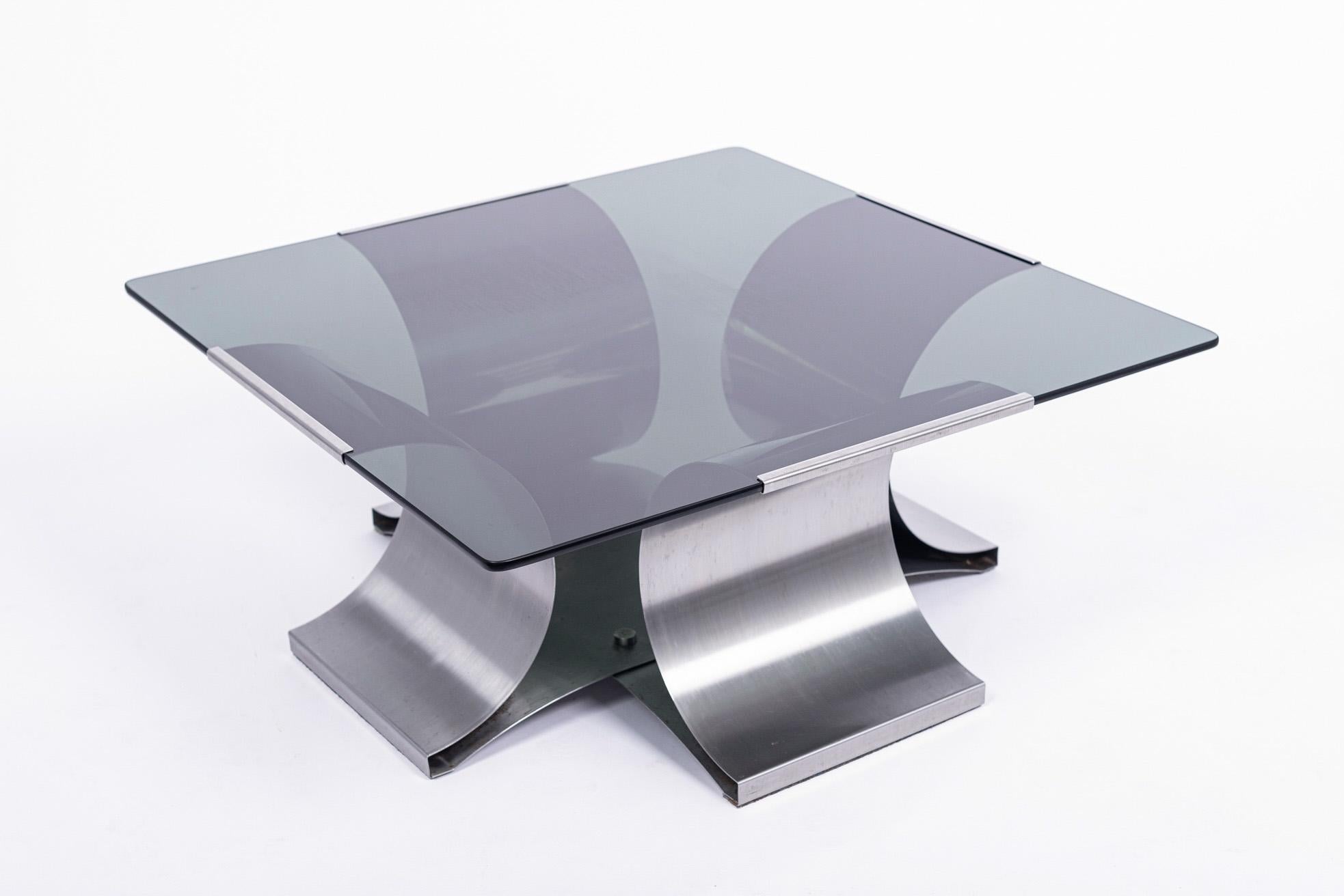 This vintage Mid-Century Modern steel and glass square coffee table designed by François Monnet for Kappa was made in France circa 1970. The inventive, Space Age design features a curved brushed stainless steel base with a 3/8” dark gray tinted