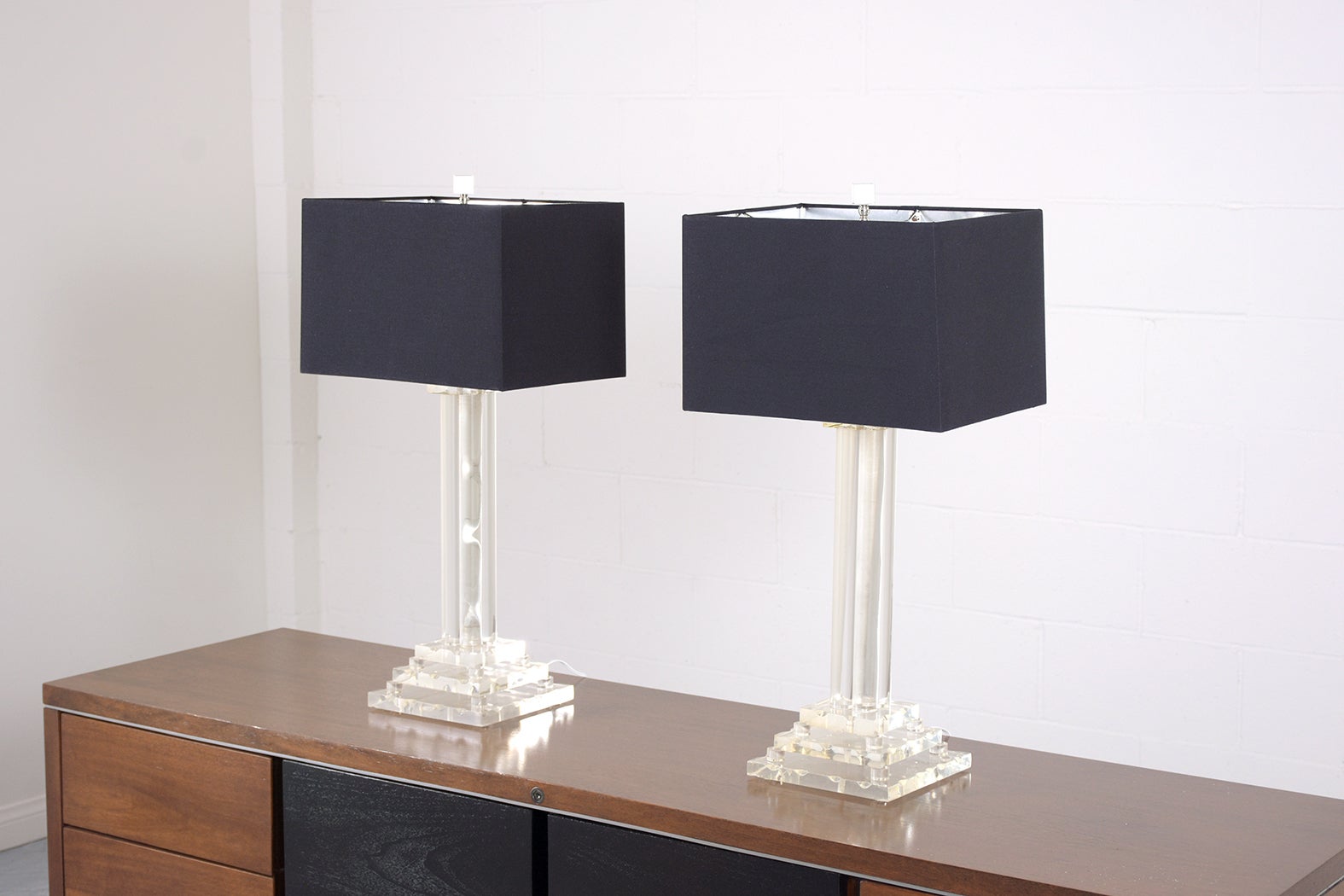 This extraordinary pair of vintage 1970s Mid-Century Modern lucite table lamps are in good condition and features a sleek four columns pedestal raised by the square base. The lamps also come with a new black fabric shade and silvered interior that