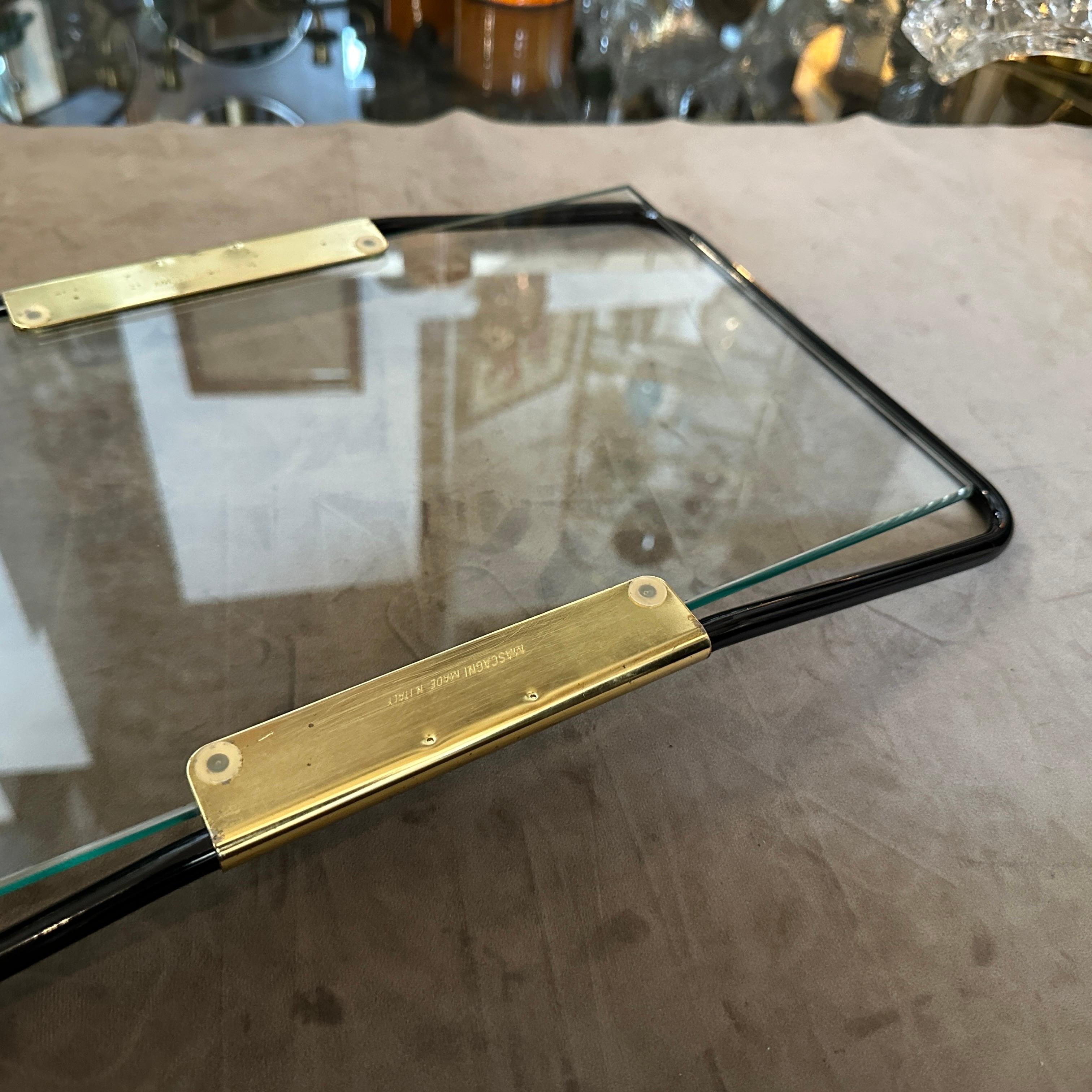 This is a 1970s Mid-Century Modern tray designed and manufactured in Italy by Umberto Mascagni. The serving tray features a sleek and minimalist design characteristic of the era, with a black-painted metal frame and polished brass accents on the
