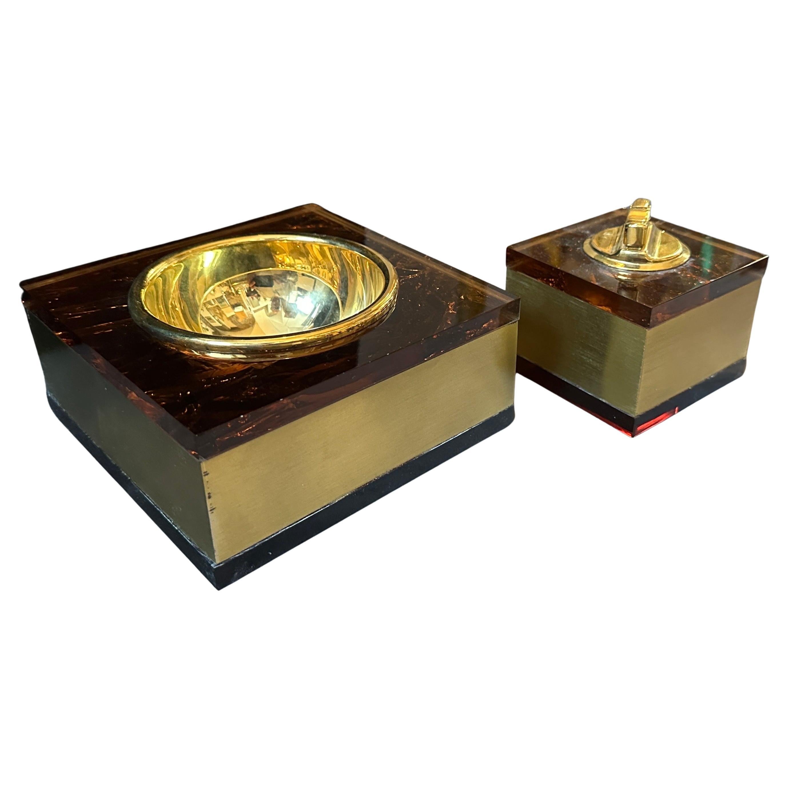 This 1970s Mid-Century Modern Italian ashtray and lighter set exudes a glamorous and sophisticated design, typical of the period's penchant for luxurious materials and bold aesthetics. The set combines brass and faux tortoiseshell Lucite, resulting