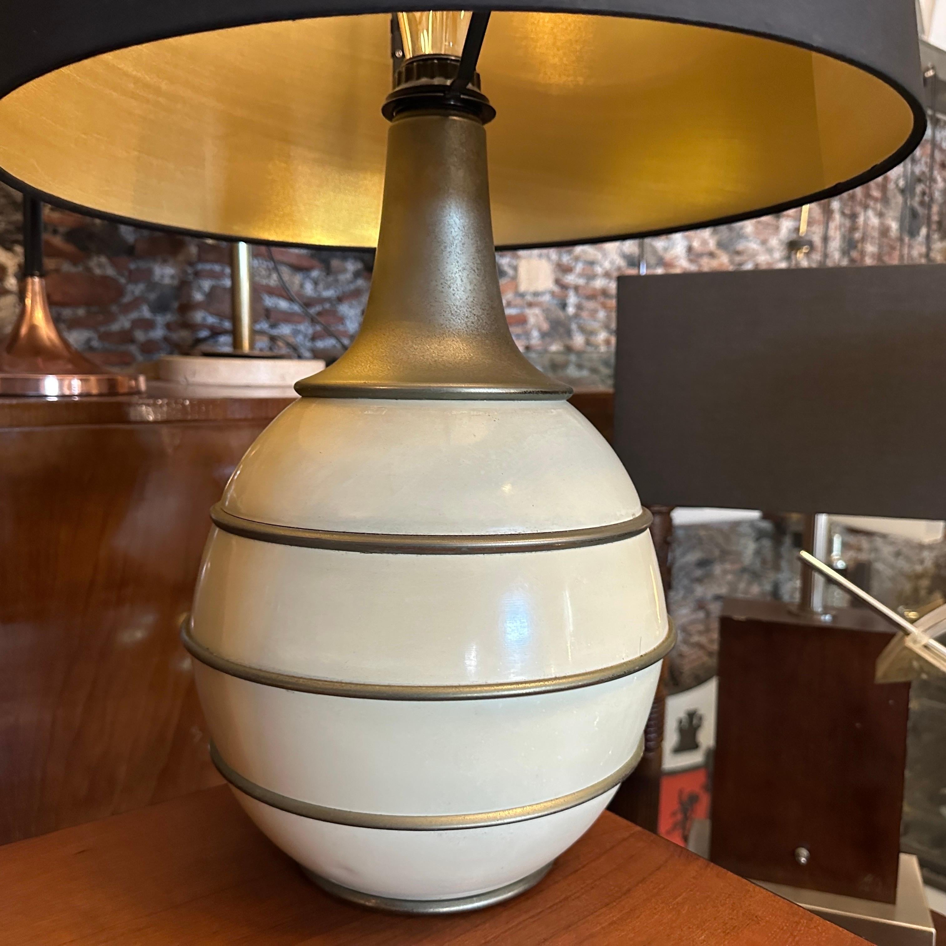 This 1970s Mid-Century Modern Italian table lamp, in the manner of Tommaso Barbi, exudes sophisticated elegance with its distinctive design. The base features a layered, bulbous form crafted from ivory lacquered metal, accented by sleek brass bands