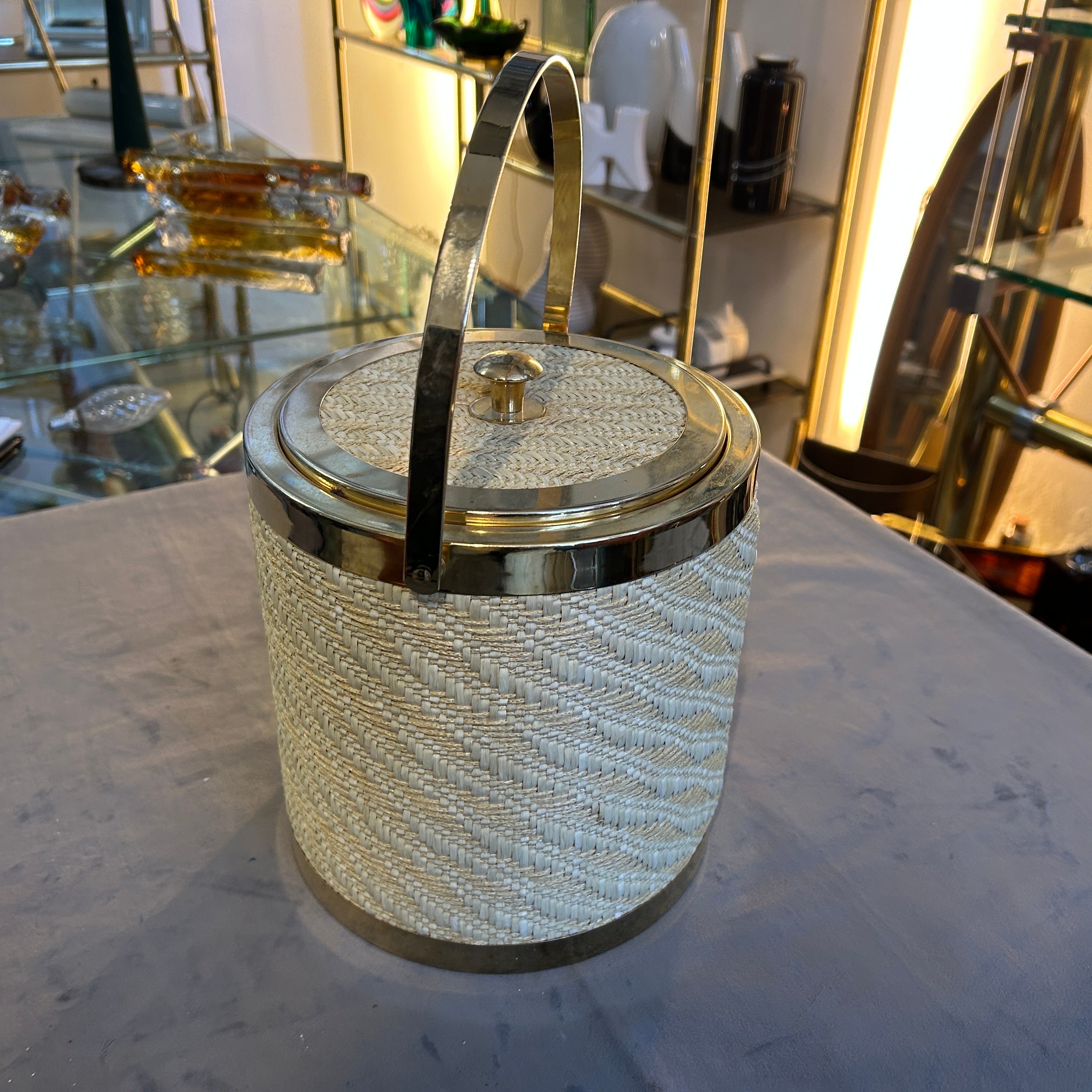 This Ice Bucket is a stylish and sophisticated piece of barware that captures the essence of its era. This ice bucket combines the sleekness of brass with the organic texture of wicker, creating a unique and eye-catching design that was highly