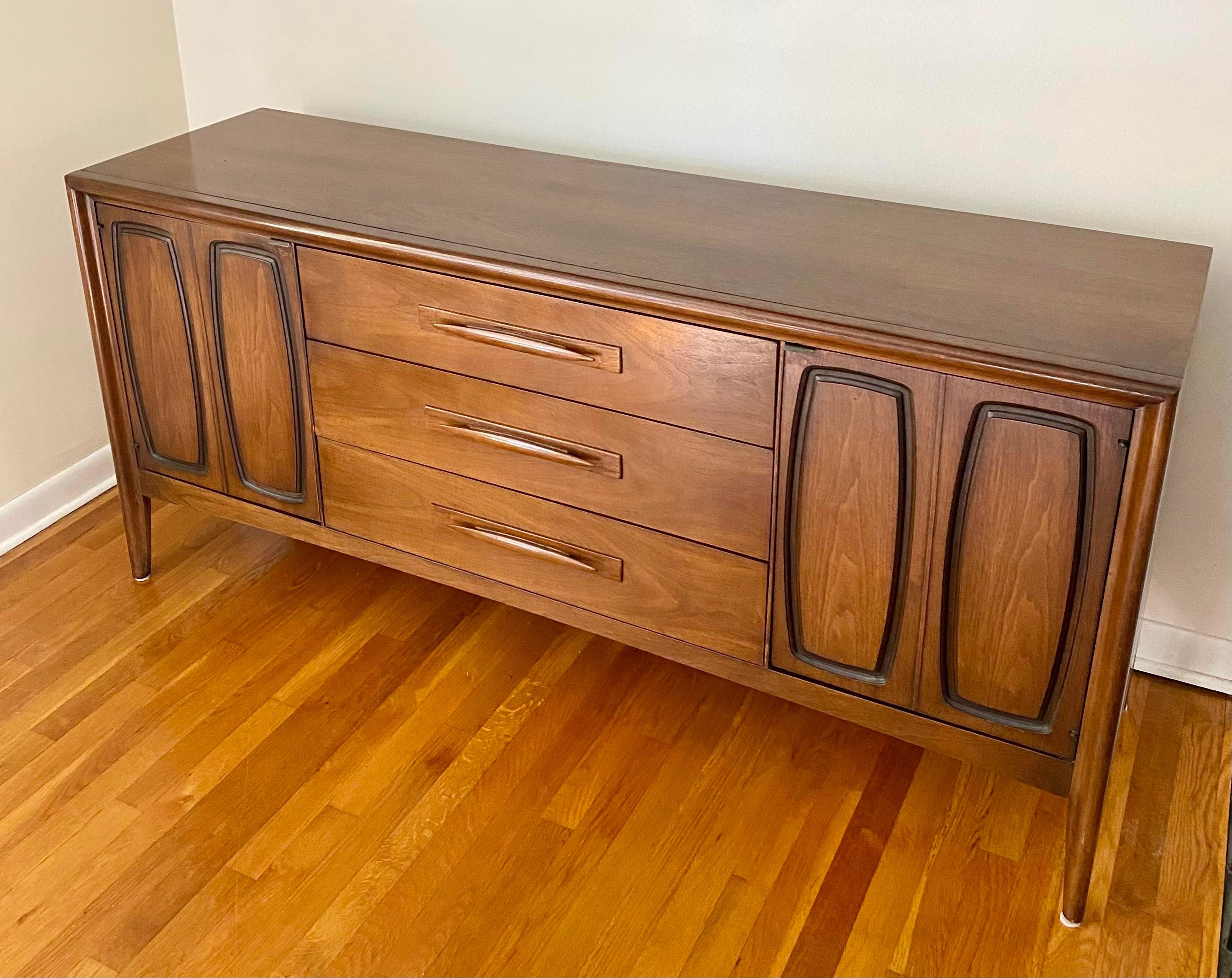 Mid-Century Modern Broyhill Emphasis Walnut Credenza features 3 pull drawers in the middle and 2 carved wooden doors on the sides.

Made by Broyhill Furniture, USA 1970s
