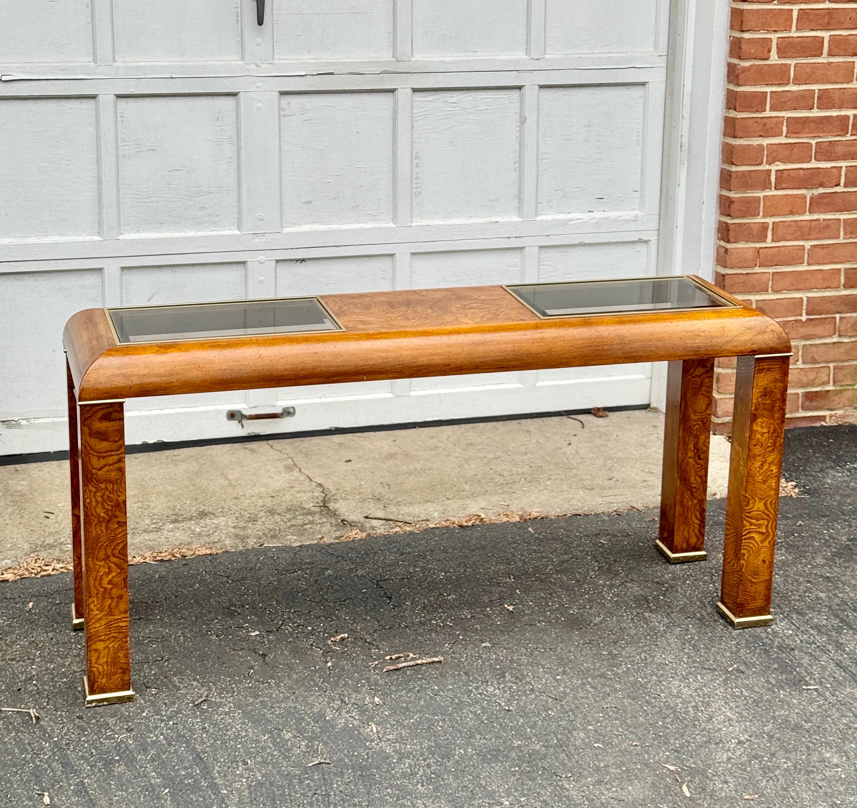 Console parsons table from the 1970s, showcasing a tasteful blend of burl wood and brass accents. Characterized by a low-profile silhouette with gently curved edges. The smoked glass tops, with beveled detailing, add a touch of refinement and can be