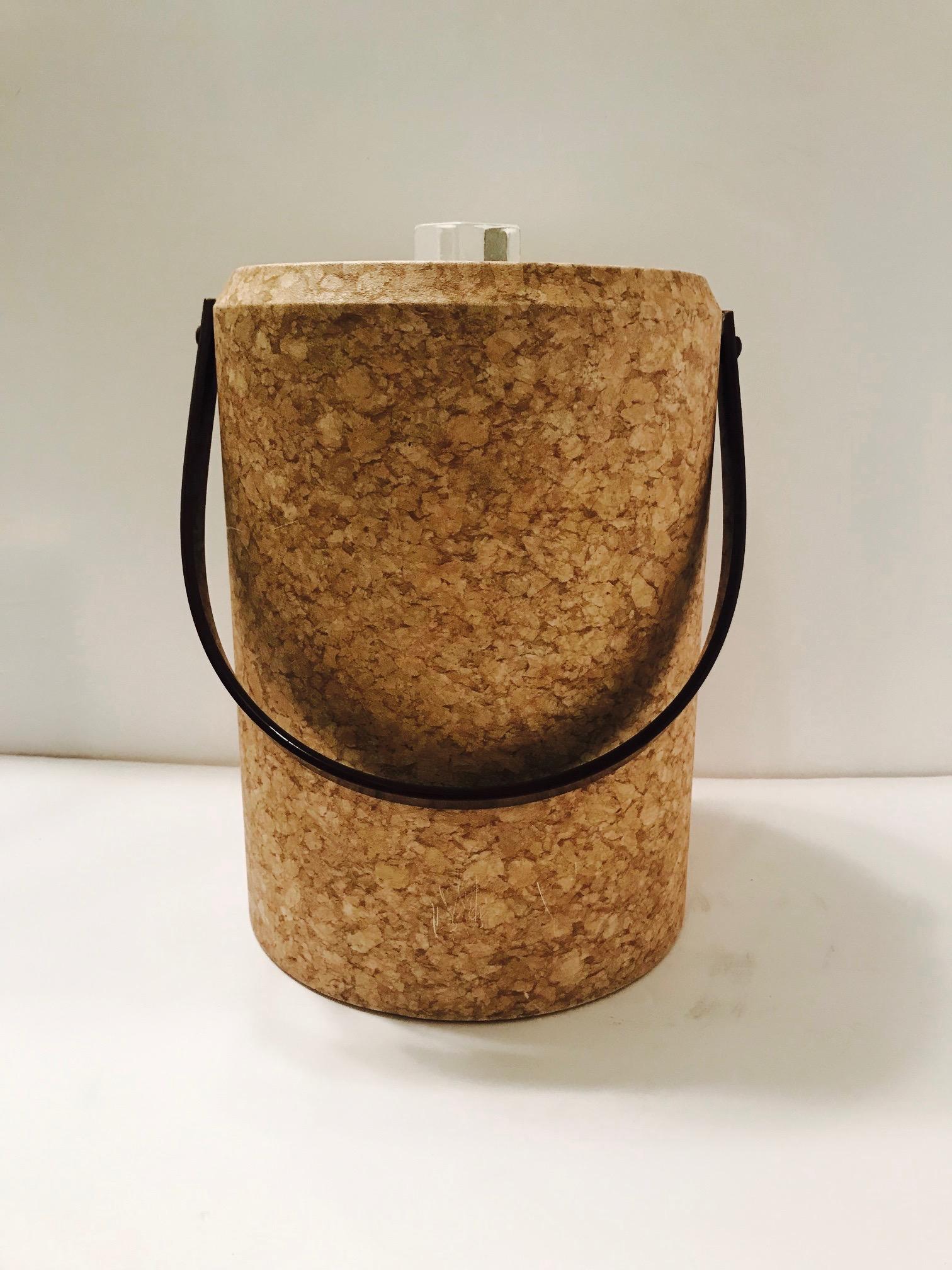 Chic 1970s acrylic ice bucket wrapped in cork design waterproof laminate. Tall cylinder form features a dark brown Lucite handle and clear Lucite lid fitted with stylized ice finial and a white acrylic interior. Indoor/outdoor use and easy to clean.