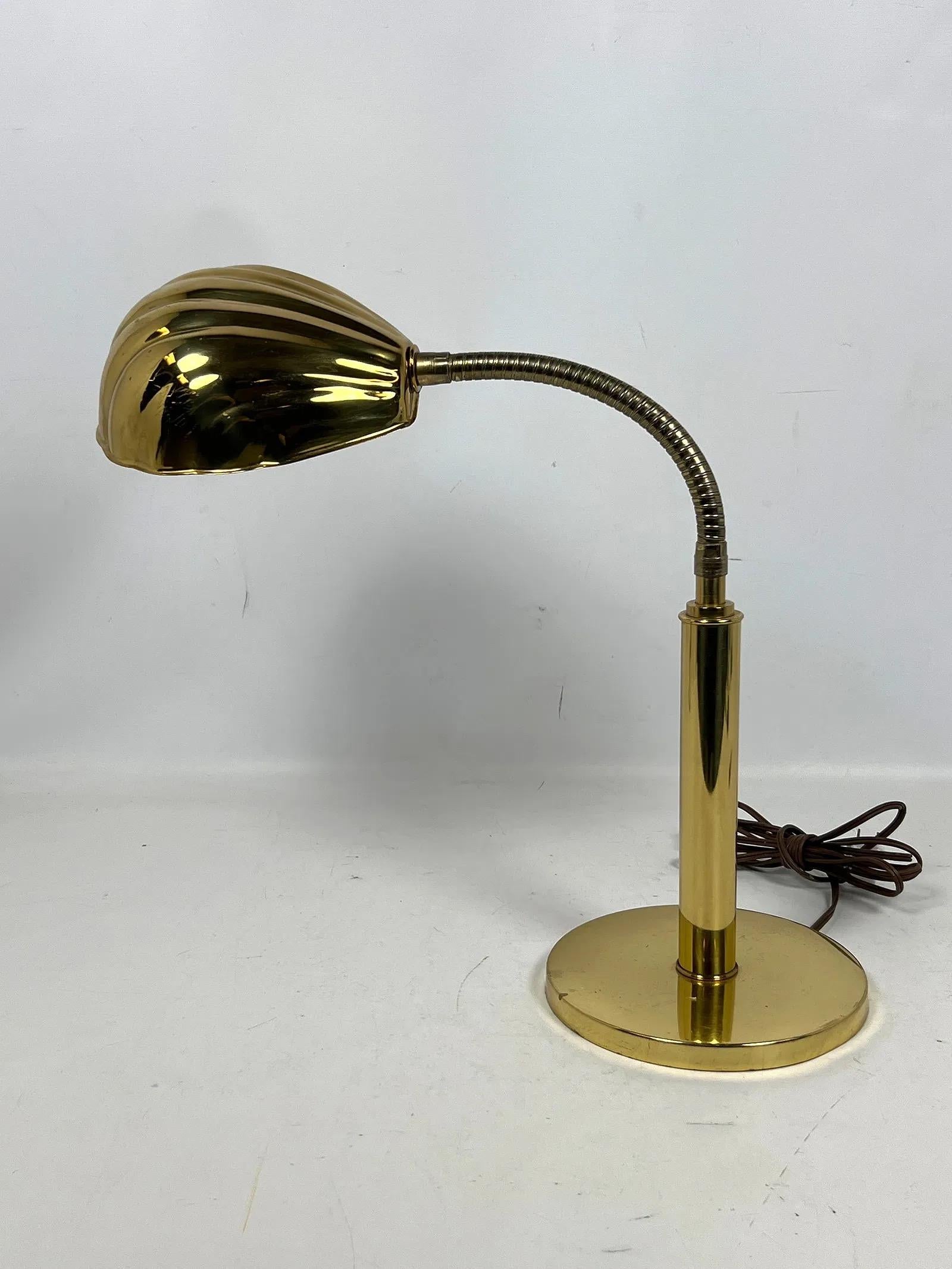 Brass gooseneck desk lamp with an elegant shell-form shade. The lamp features a flexible, curved arm that allows for adjusting the shade’s direction, making it perfect for reading, writing, or detailed work.
