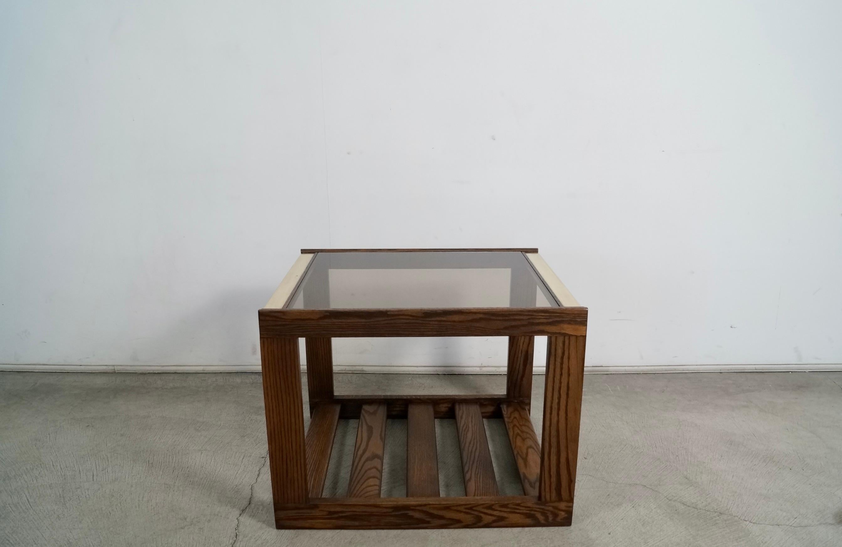 Vintage Midcentury Modern end table for sale. Manufactured in the 1970's, and has been professionally refinished in walnut. It's made of solid oak, and has a walnut finish. It has brass trims on the surface, and a smoked dark glass insert. It has a