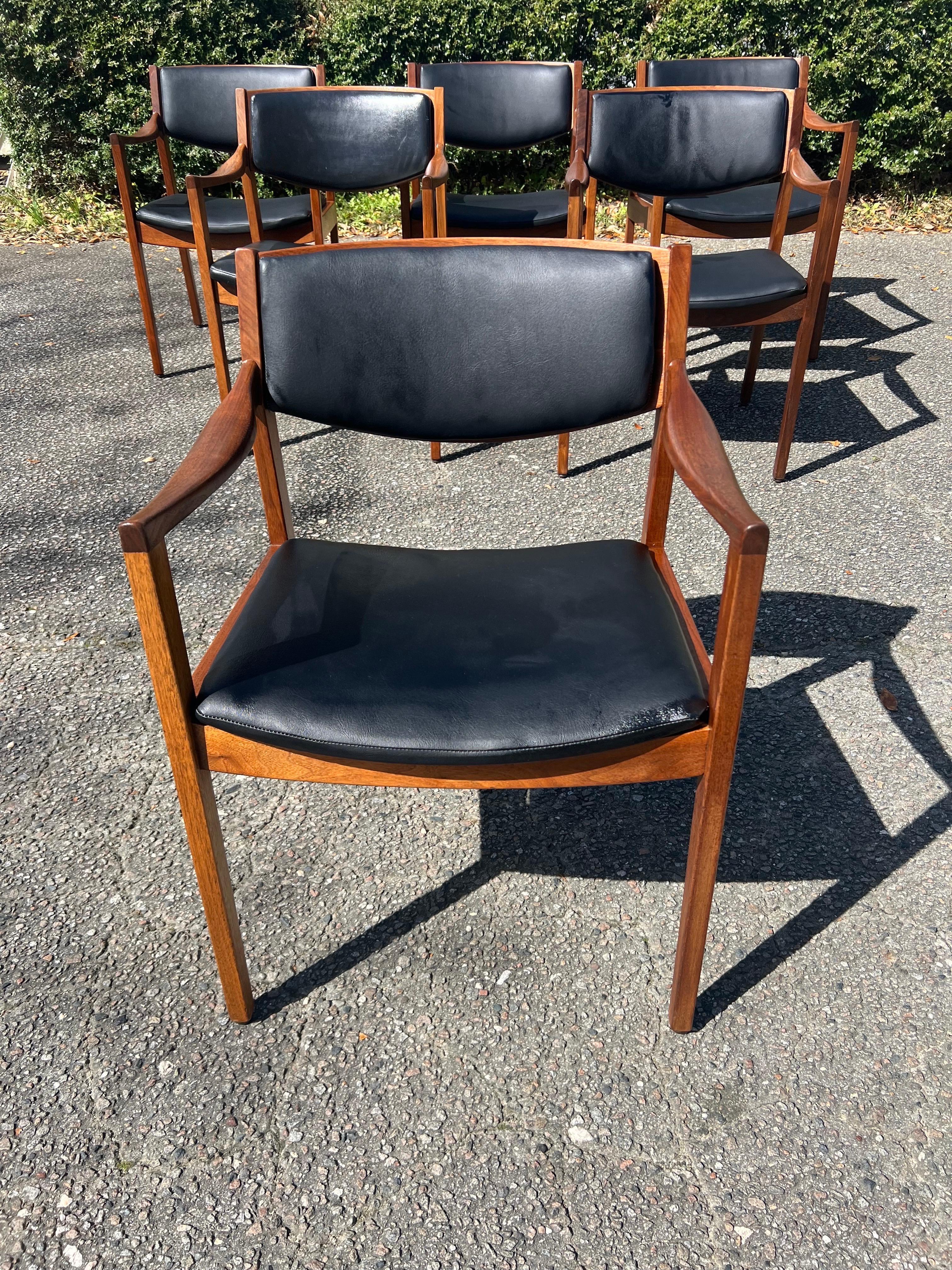 These mid-century modern Gunlocke armchairs feature solid wood construction, sculpted walnut armrests,  and original black vinyl upholstery. With swooped armrests, these beautifully designed accent chairs  are in excellent vintage condition with one