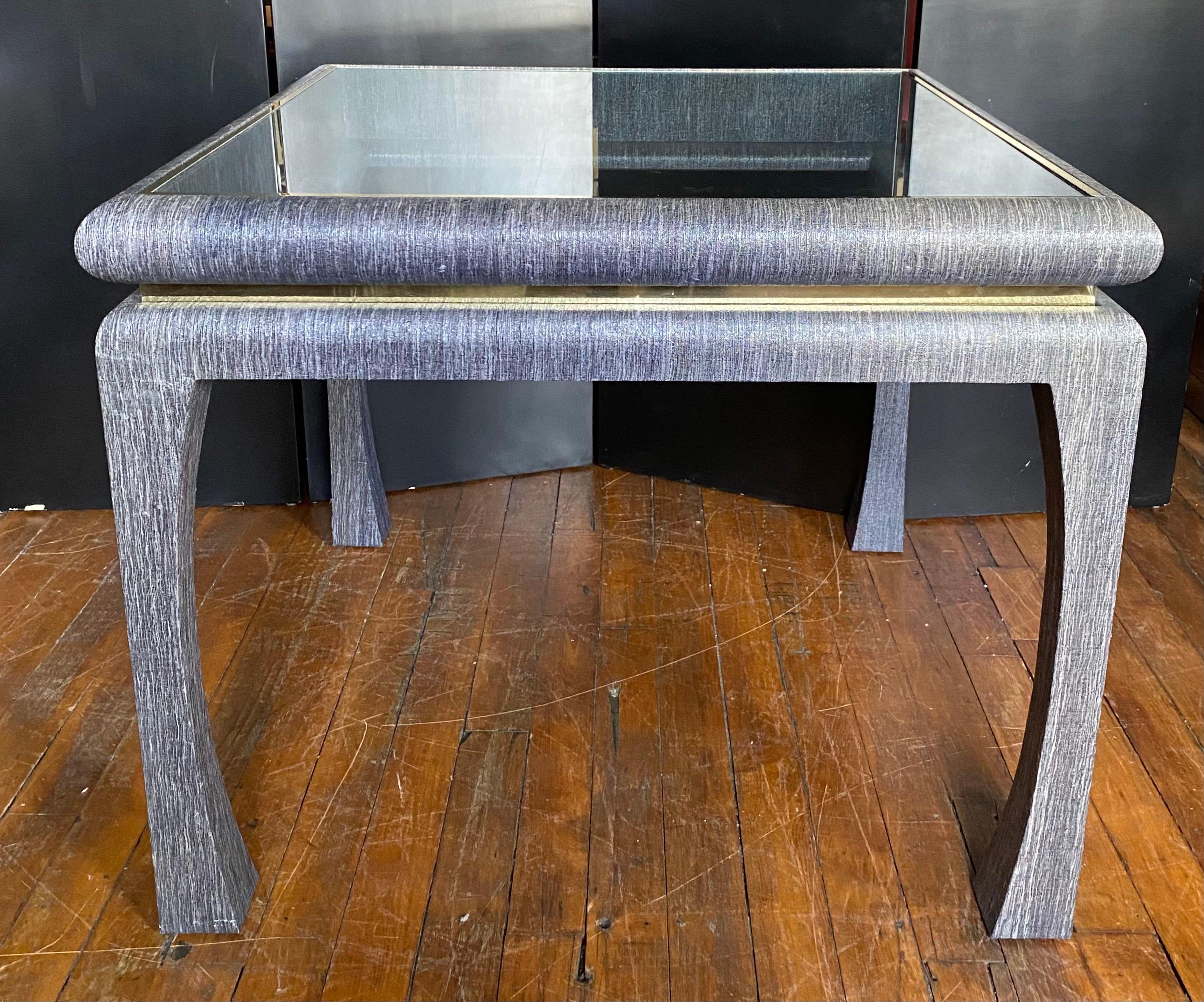 Mid Century Modern linen grasscloth card or game table. This square shaped wood table is wrapped in a deep blue-grey charcoal textural glazed grasscloth. The clear glass top if removable and is trimmed in gold. The table base features reflective