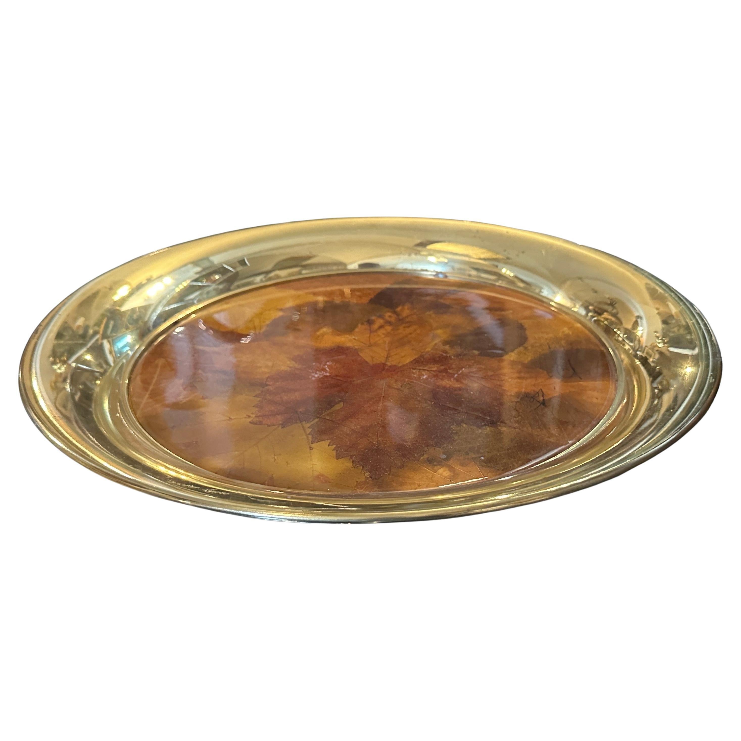 Ce plateau rond italien des années 1970 est un bel exemple du design moderne du milieu du siècle, combinant de manière frappante des éléments organiques et métalliques. Le plateau présente un bord en laiton poli qui entoure une surface en Lucite,