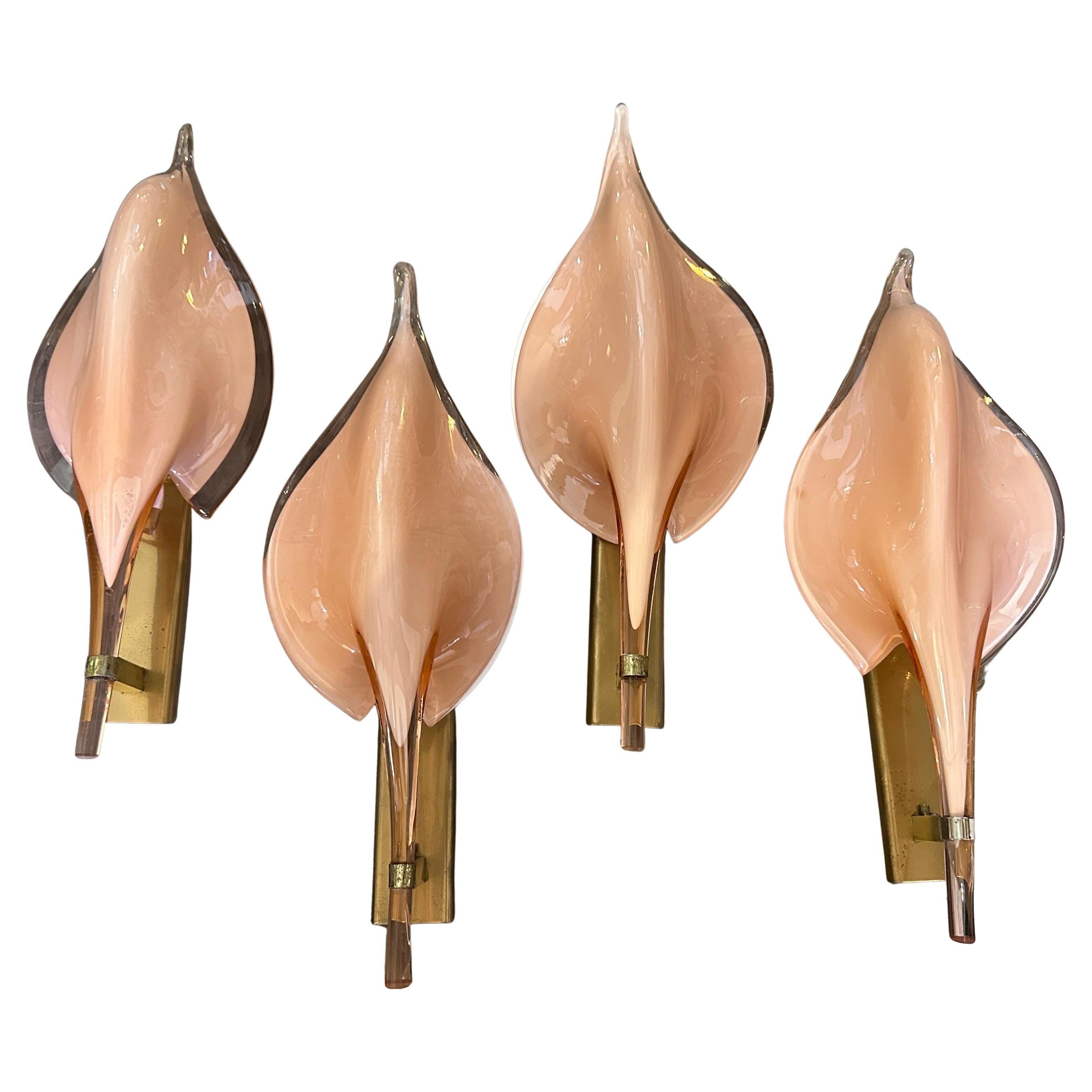 These are 1970s Mid-Century Modern wall sconces designed by Franco Luce. The sconces feature a striking leaf-shaped design made of hand-blown pink Murano glass, with a translucent finish and soft curves that create a warm inviting glow. The elegant