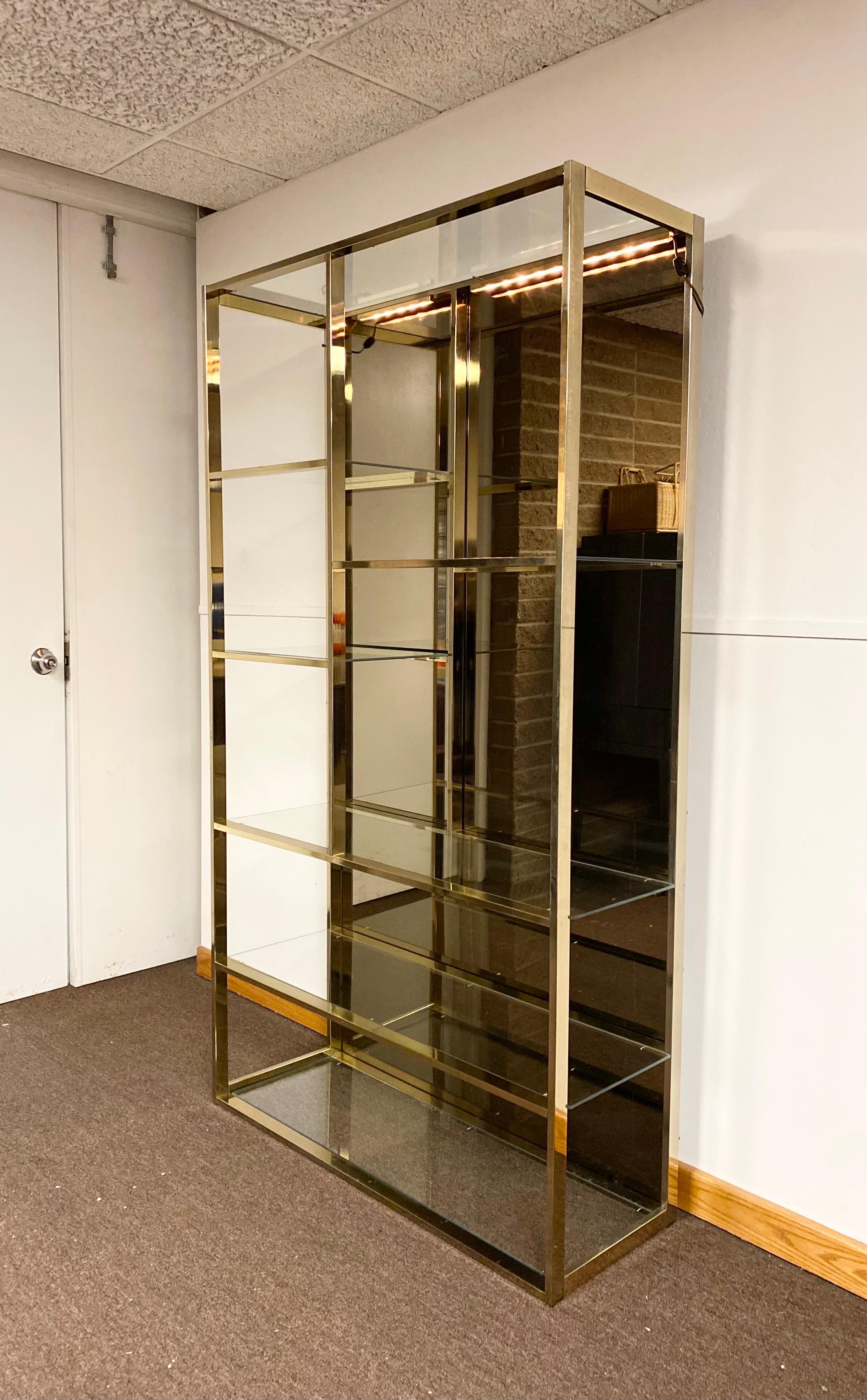 We are very pleased to offer a stunning etagere, circa the 1970s. Beautiful polished brass, a smoky mirrored interior back panel and clear glass come together to form a streamlined piece for storage and display. Perfect for any décor due to its