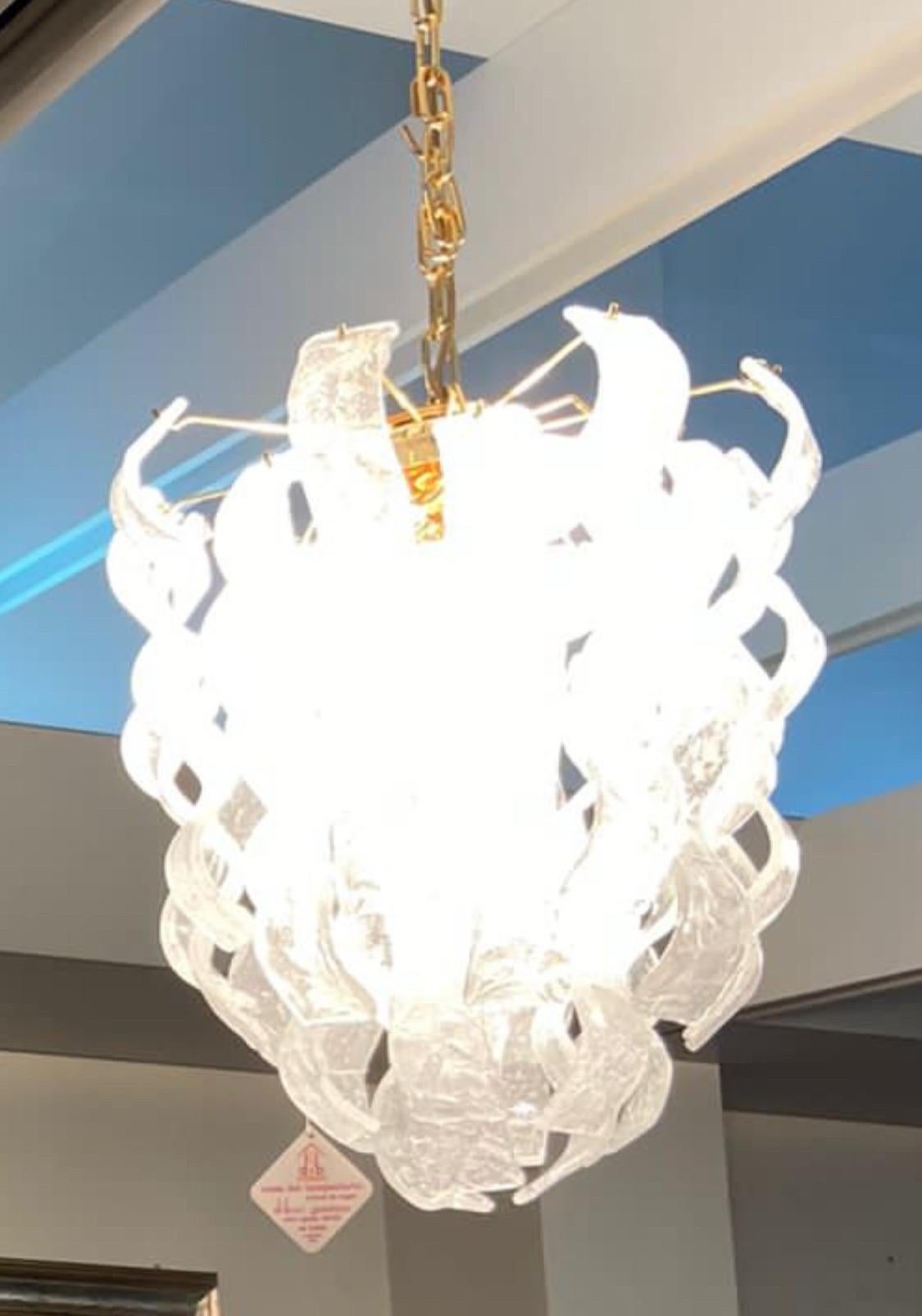 Un étonnant lustre en verre Murano blanc givré, conçu et fabriqué en Italie dans les années soixante-dix. Composé d'éléments en métal doré et en verre de Murano glacé, il n'a jamais été utilisé car il provient d'un important magasin de luminaires en