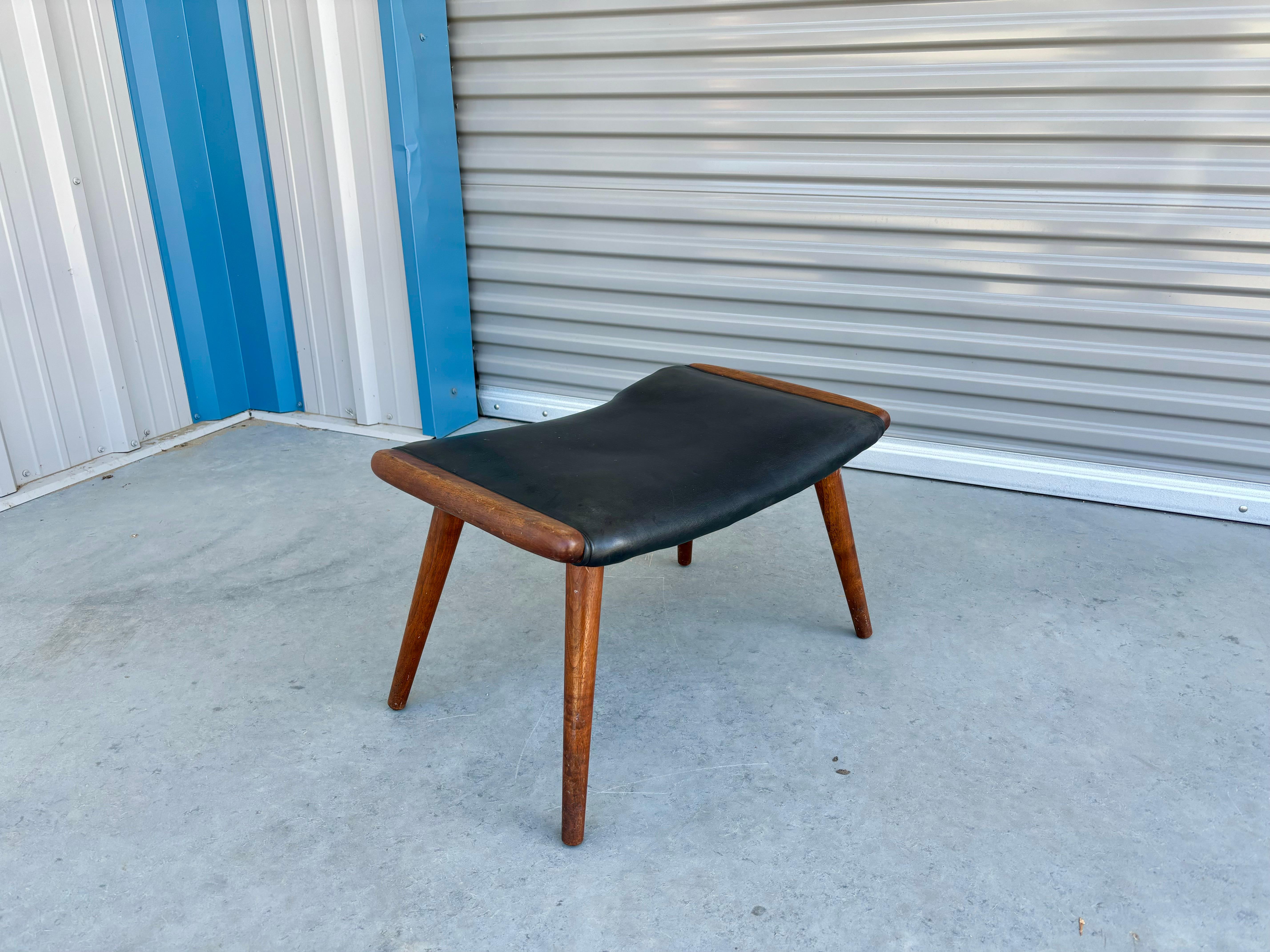 Mid Century papa bear ottoman designed and manufactured in the United States circa 1970s. This stunning stool exudes elegance and sophistication with its sleek black leather upholstery that perfectly complements the rich tones of the teak frame.