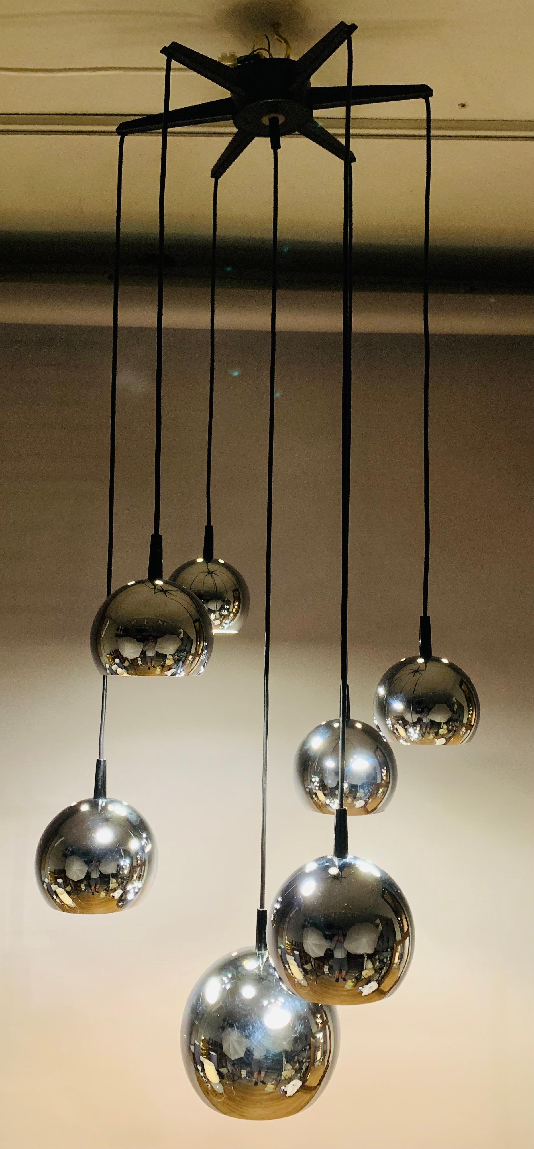 1970s, German, space-age, hanging ceiling light with seven cascading chrome globes each suspended from a black wire flex and a star ceiling canopy. The light has three varying sizes of globe - 3 small, 3 medium nd one large one at the very bottom.
