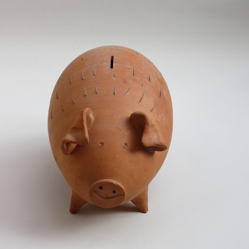 Wonderful hand made large stylised terracotta pig shaped piggy bank from the 1970s.

Coin slot to the top, no access to the coins, this is a fill and break piggy bank. Very nice character to the pig, good decorative piece.
Very good condition, no