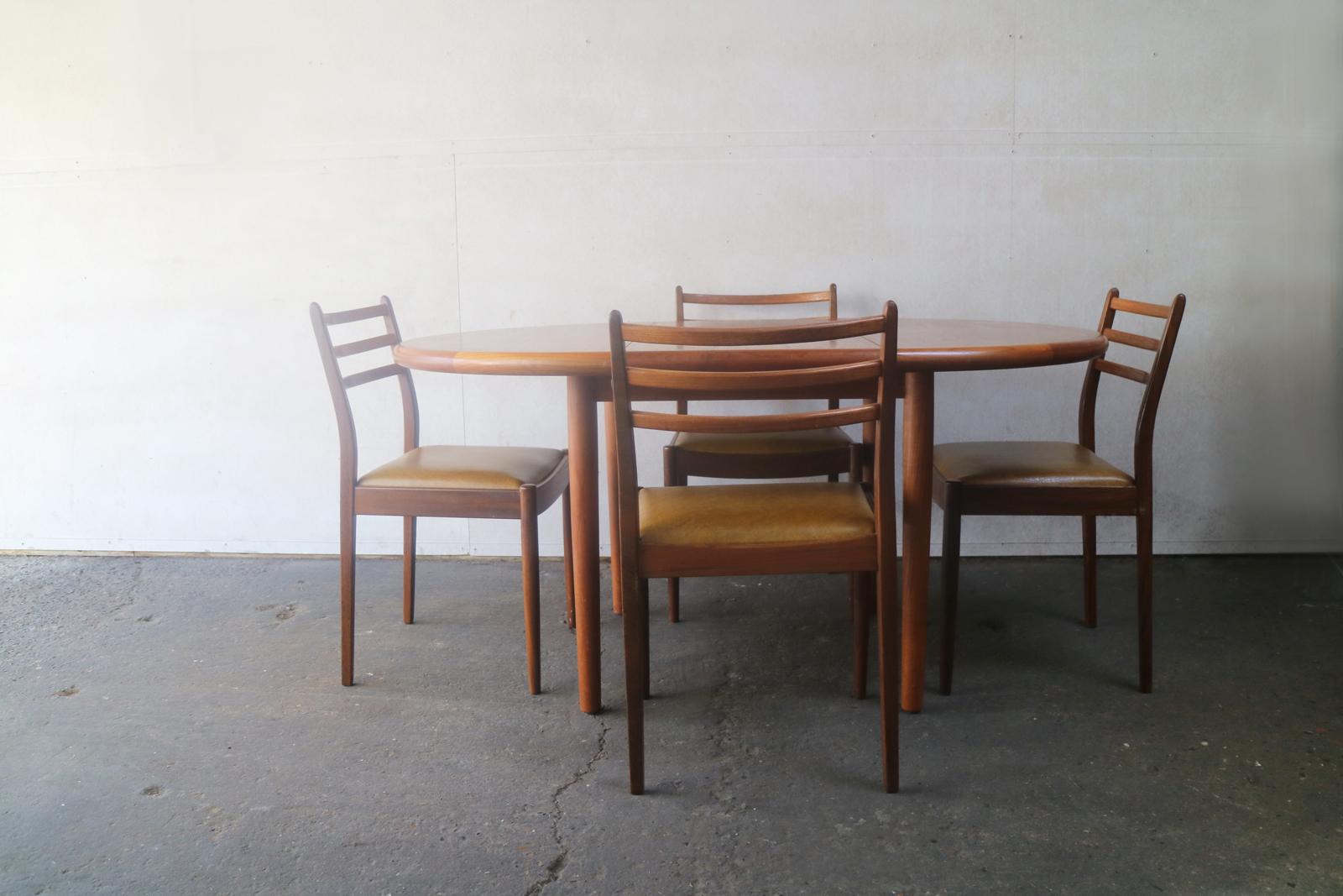 A very fine, relatively small extending Danish dining table with lovely wood grain, thick rounded edges and decorative inlaid edging. The G Plan chairs are elegant, with dark teak frames and mustard colored vinyl seating.

Table is stamped ‘Made