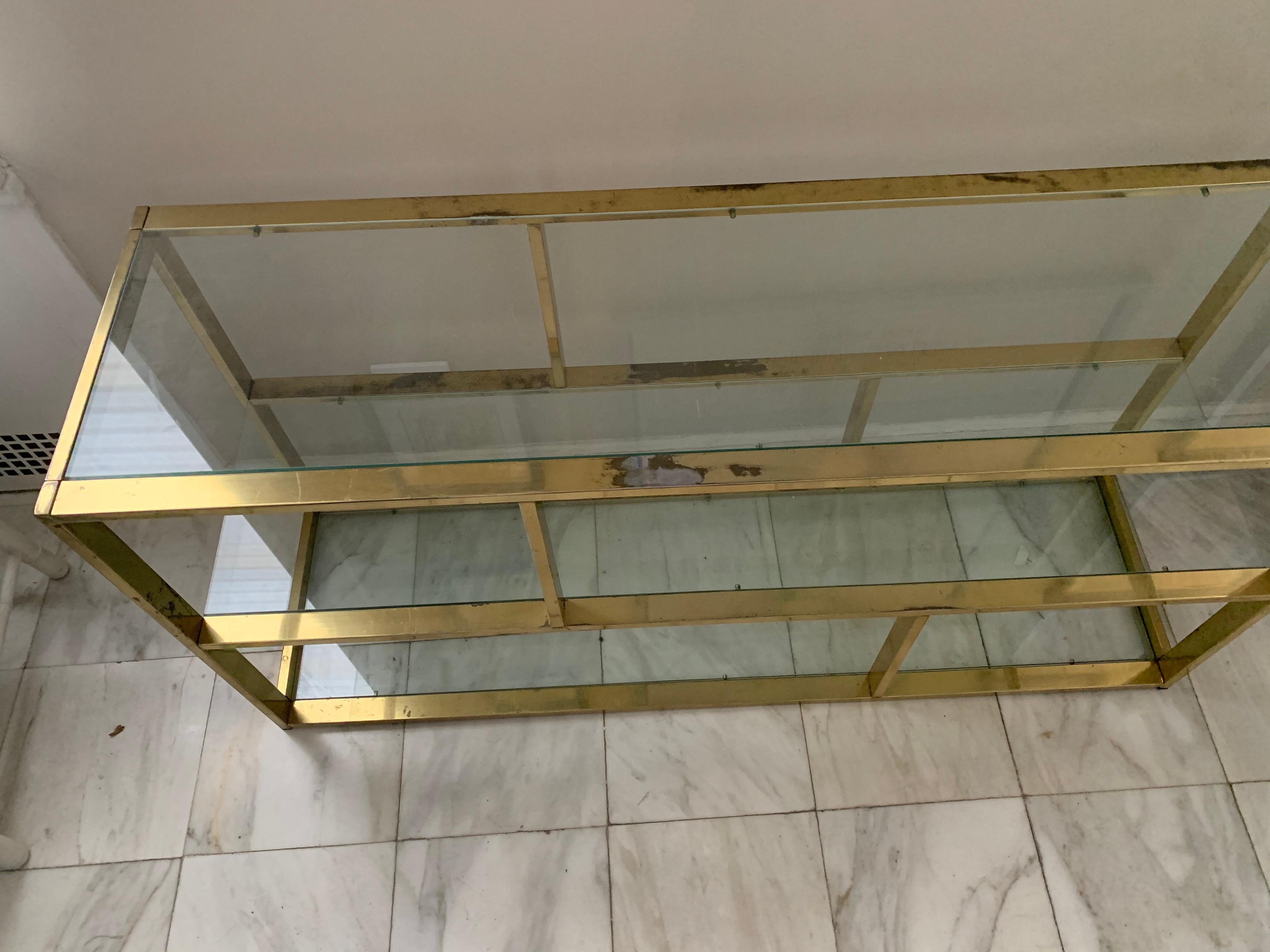 1970s Milo Baughman brass and glass low bookshelf or etagere. Solid flat bar brass frame with three clear glass shelves. 
Brass has as found overall unpolished patina.