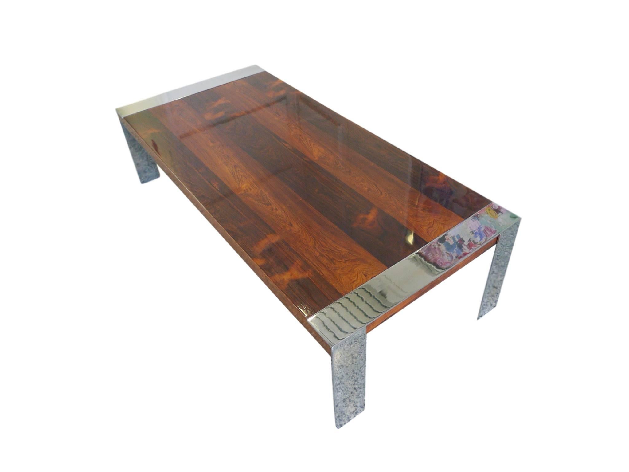 This Milo Baughman style coffee table is comprised of a rosewood tabletop and chrome legs. The rosewood is newly refinished. It has deep red-brown bands that follow the width of the table. The legs are thin, flat bars of chrome that give the