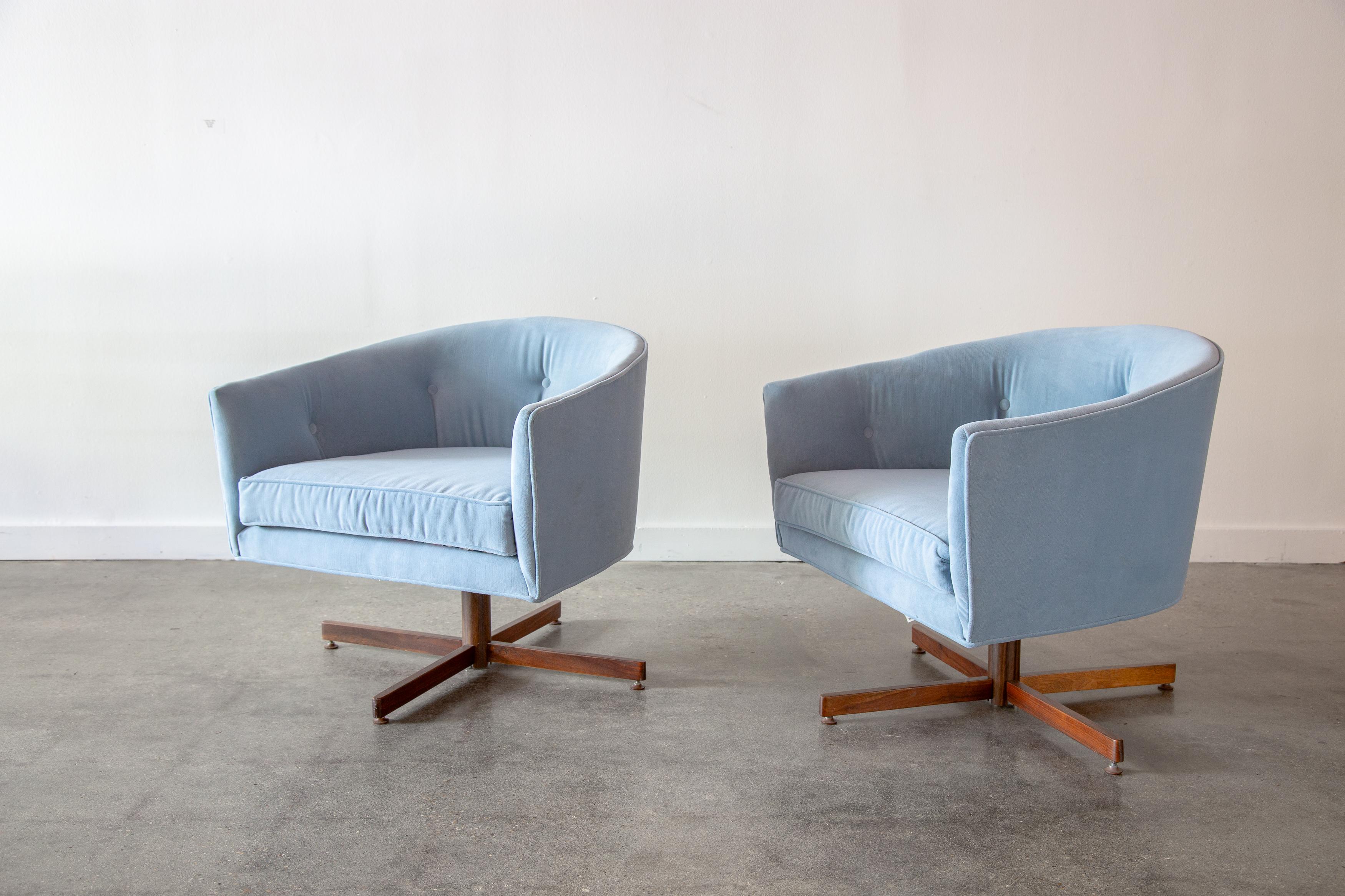 A pair of 1970s swivel tub chairs designed by Milo Baughman for Thayer Coggin. Upholstered in a baby blue velvet upholstery with reversible cushions with a period fun and funky flower design.  These chairs swivel over walnut pedestals and have