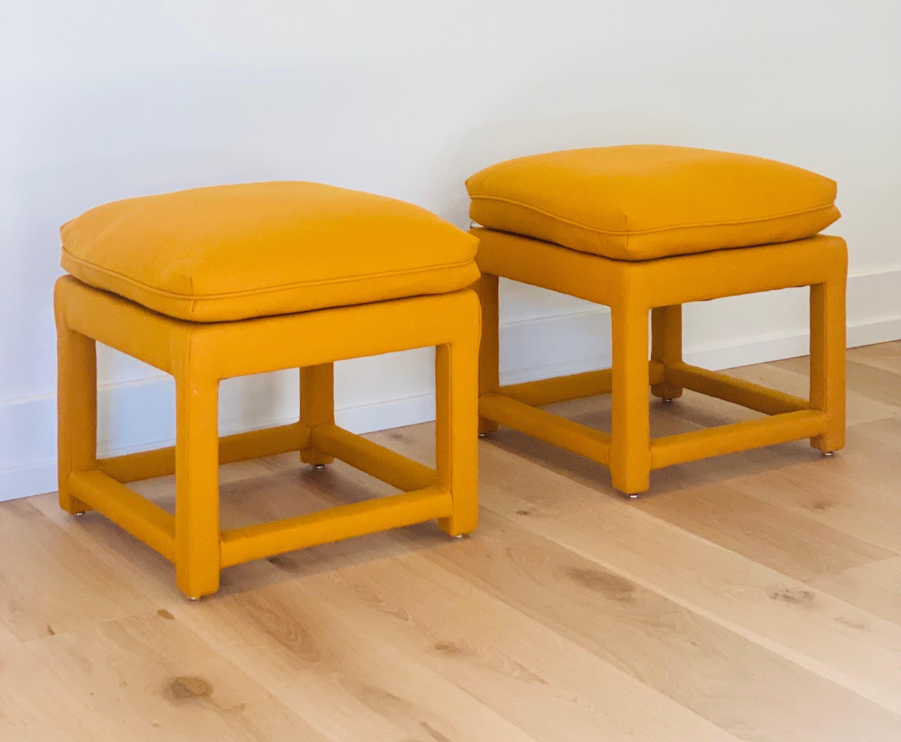 We are very pleased to offer a chic, vintage pair of Milo Baughman style ottomans, circa the 1970s. Layer a space or add extra seating with these eye-catching ottomans wrapped in a new Maharam wool, mustard color fabric. In excellent condition and