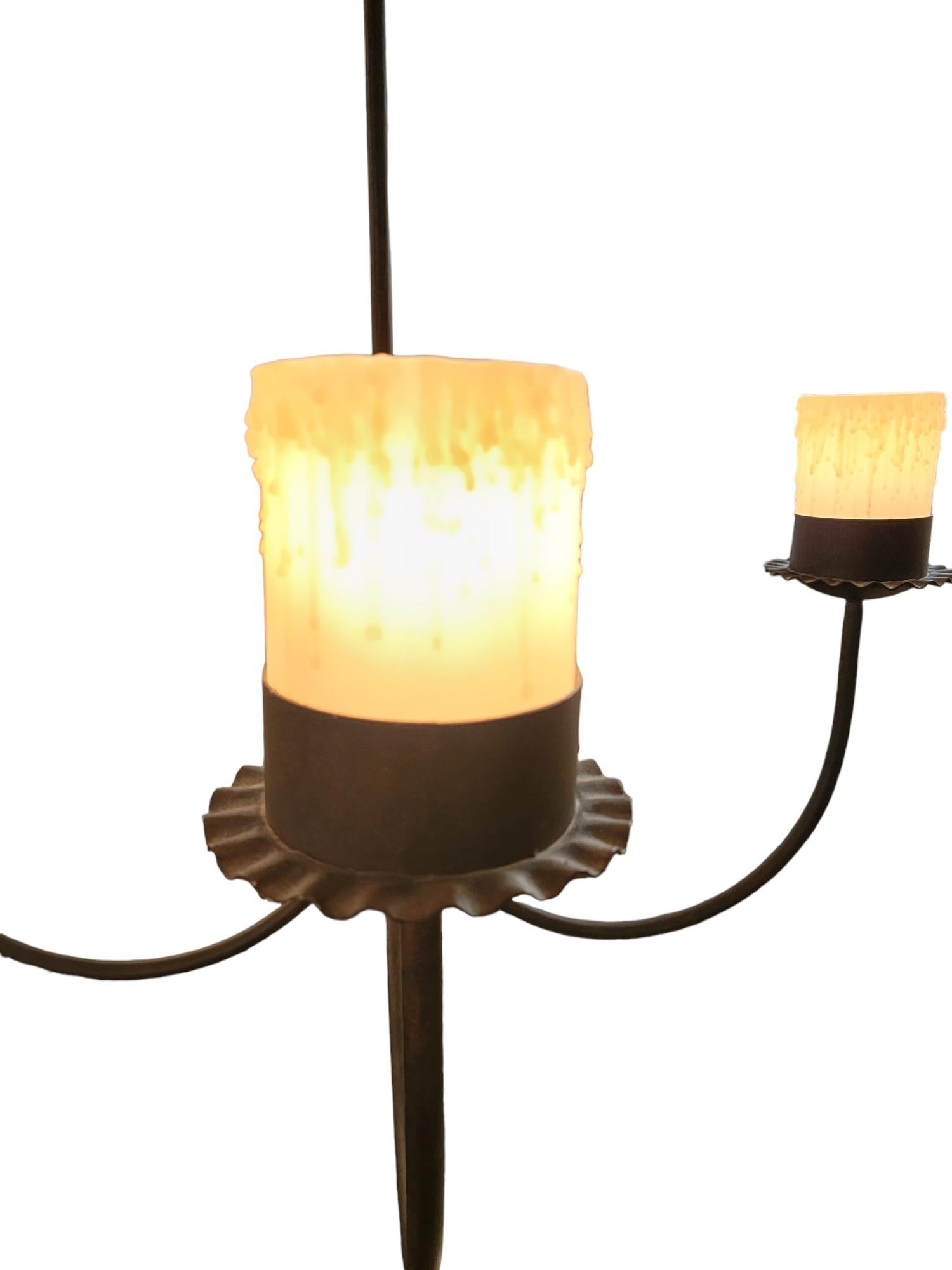 Iron 4 light 4 arm chandelier with wax candle shades with electrically lit lighting. The hook shaped arms extend generously outward and offer a glow through the wax shades when lit.