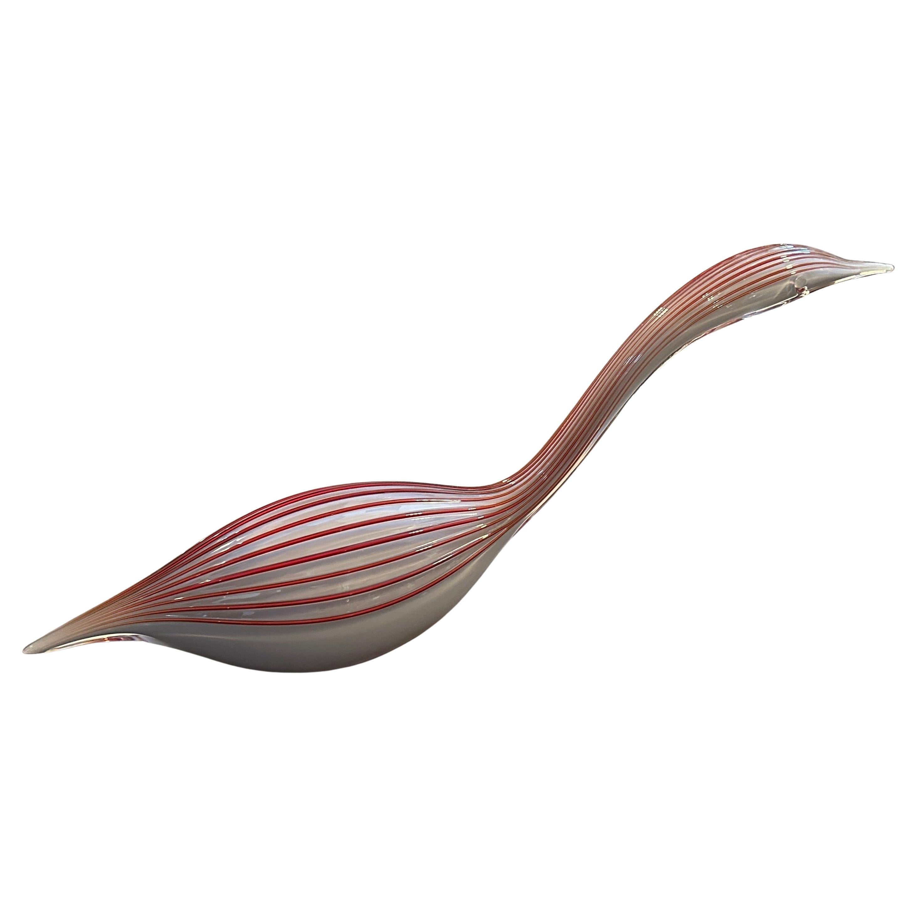 Il pezzo è una moderna scultura in vetro di Murano degli anni '70, raffigurante un'anatra. Presenta una forma allungata e slanciata con un corpo traslucido grigio/bianco ornato da suggestive linee parallele rosse che creano un effetto a strisce,