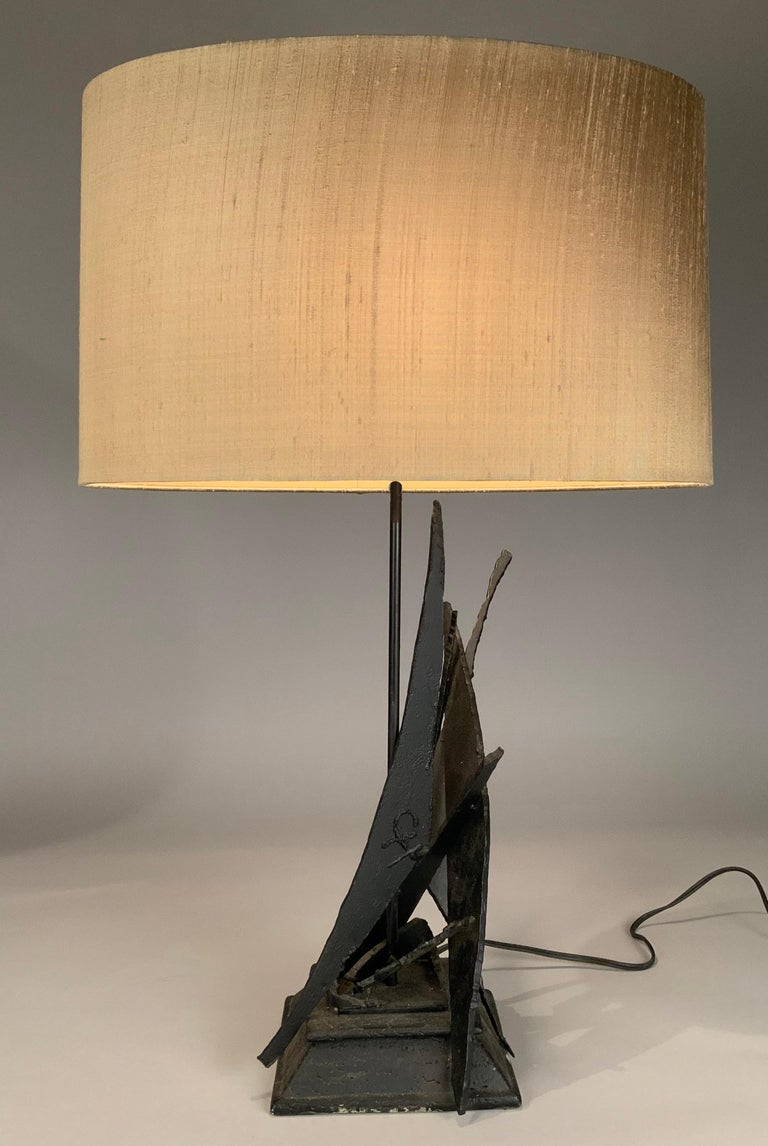 a vintage 1970's modern table lamp, with a sculpture base made from torch cut forged iron and steel, resembling sails in an abstract way. along with its original oval lampshade in mushroom color silk.