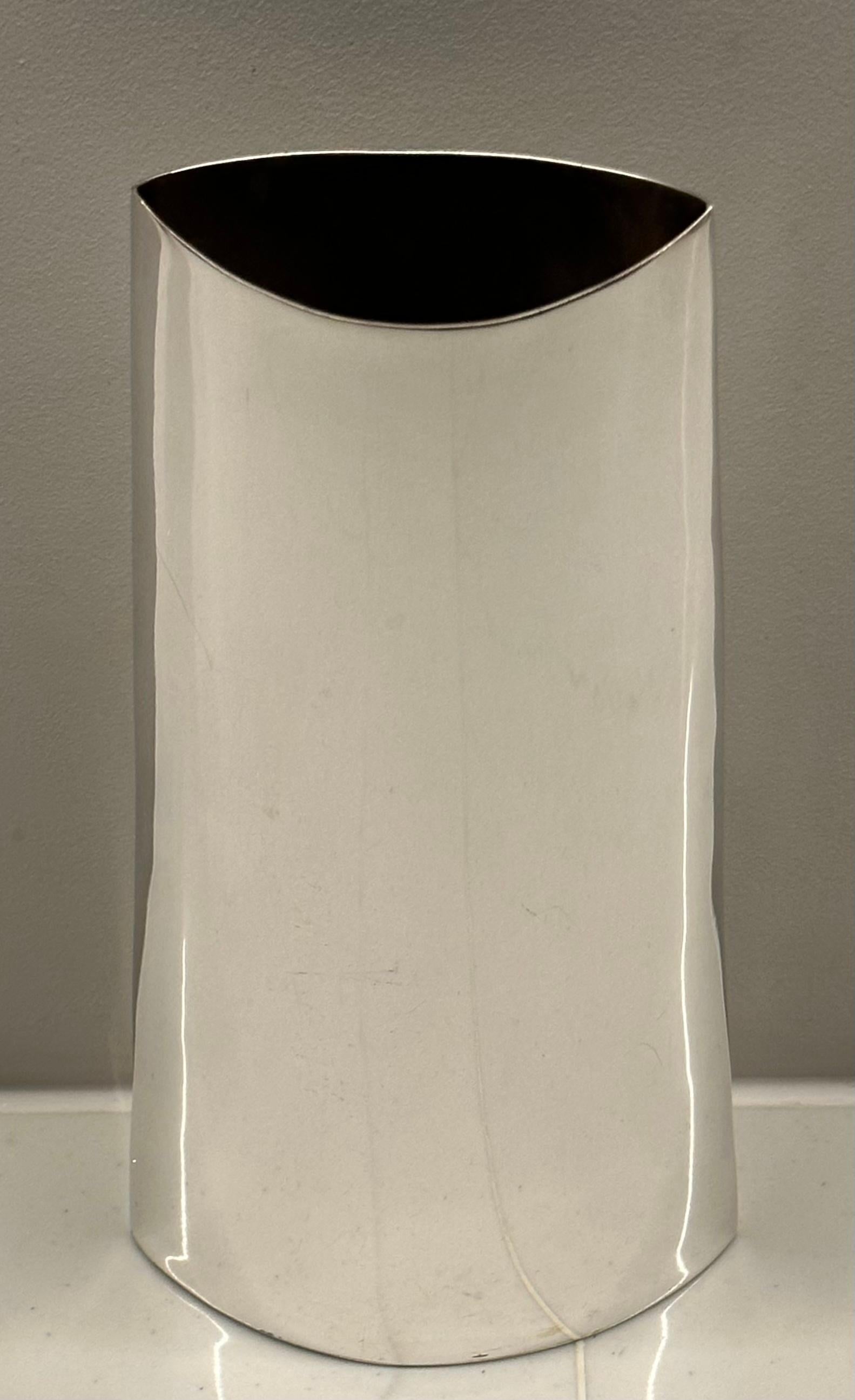 Vase italien en métal argenté des années 1970, de forme incurvée, avec une base plus large et un sommet plus étroit. Il présente une surface lisse et polie et un design simple et élégant. 

Le vase a une ouverture évasée de 4,5 cm de large et 8,5 cm