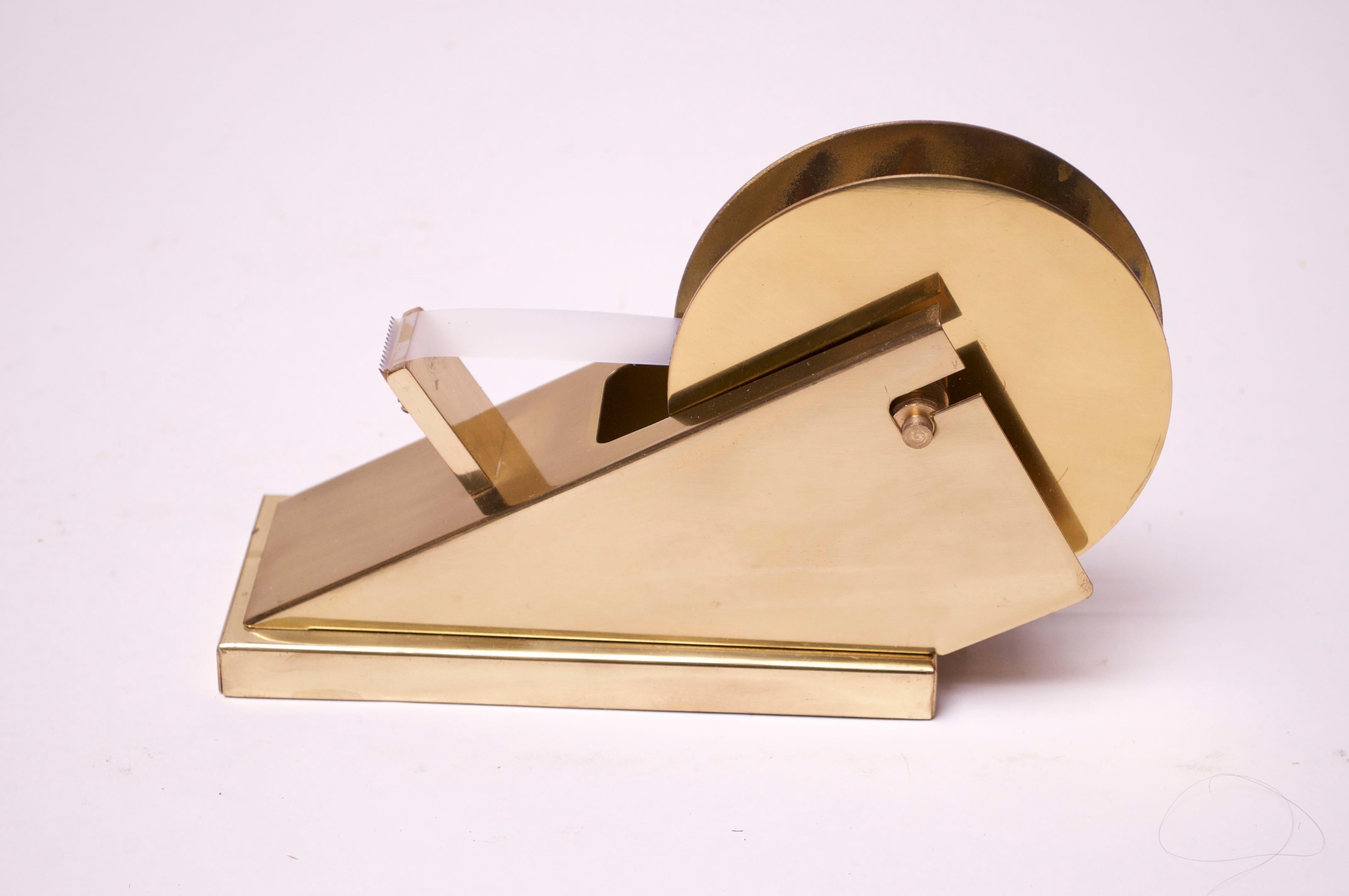 Modernist tape dispenser circa (1970s USA) in polished brass. The circular disks that hold the roll of tape in place adjust to accommodate different sized rolls. There are some lines of tarnish to the interior circular plate (can only be subtly