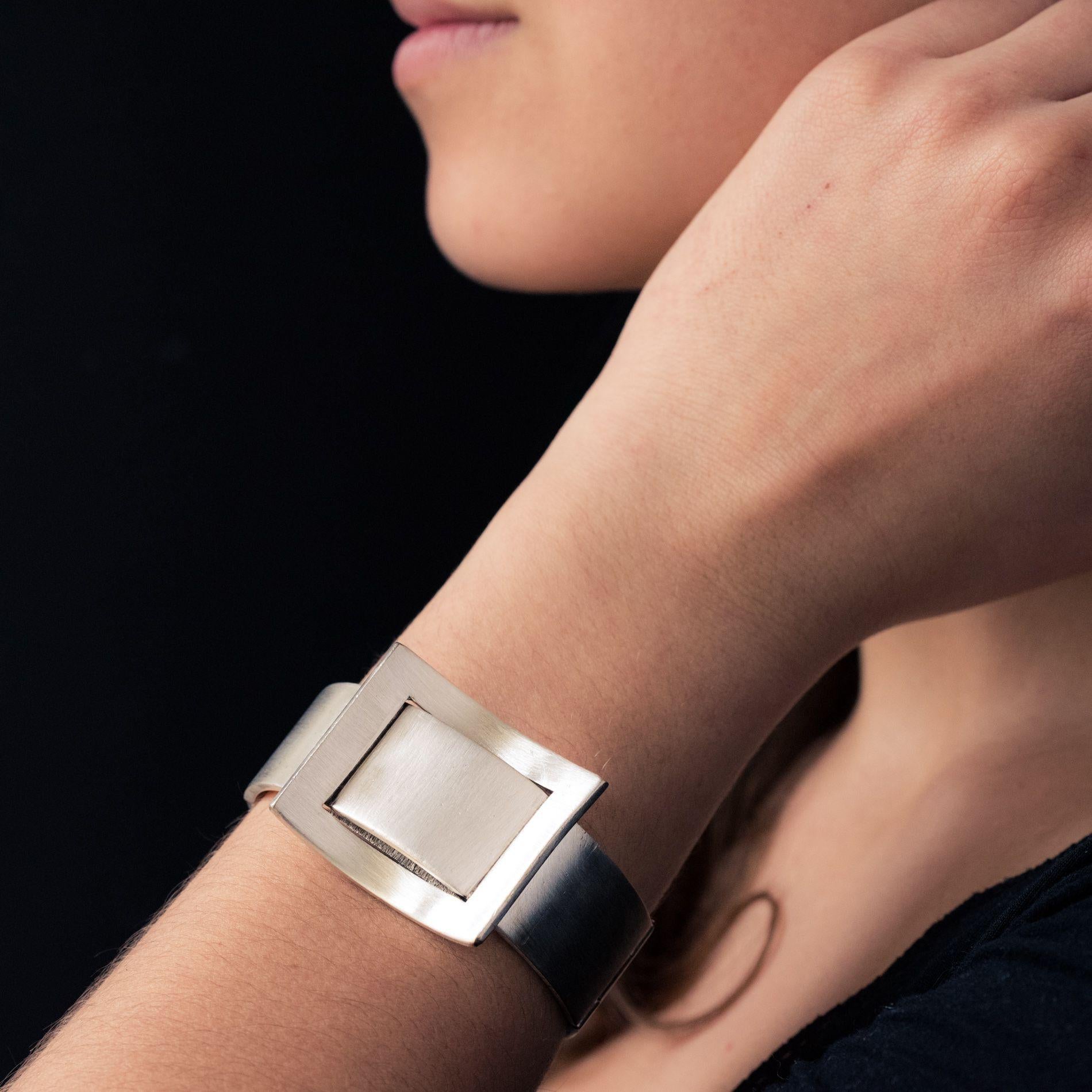Lady's watch bracelet in silver.
Large flat bangle, it has on the top a knot of geometrical shape that hides a round dial within a chiselled decoration.
Amati cream background, black enamelled Roman numerals and hands.
The entourage is