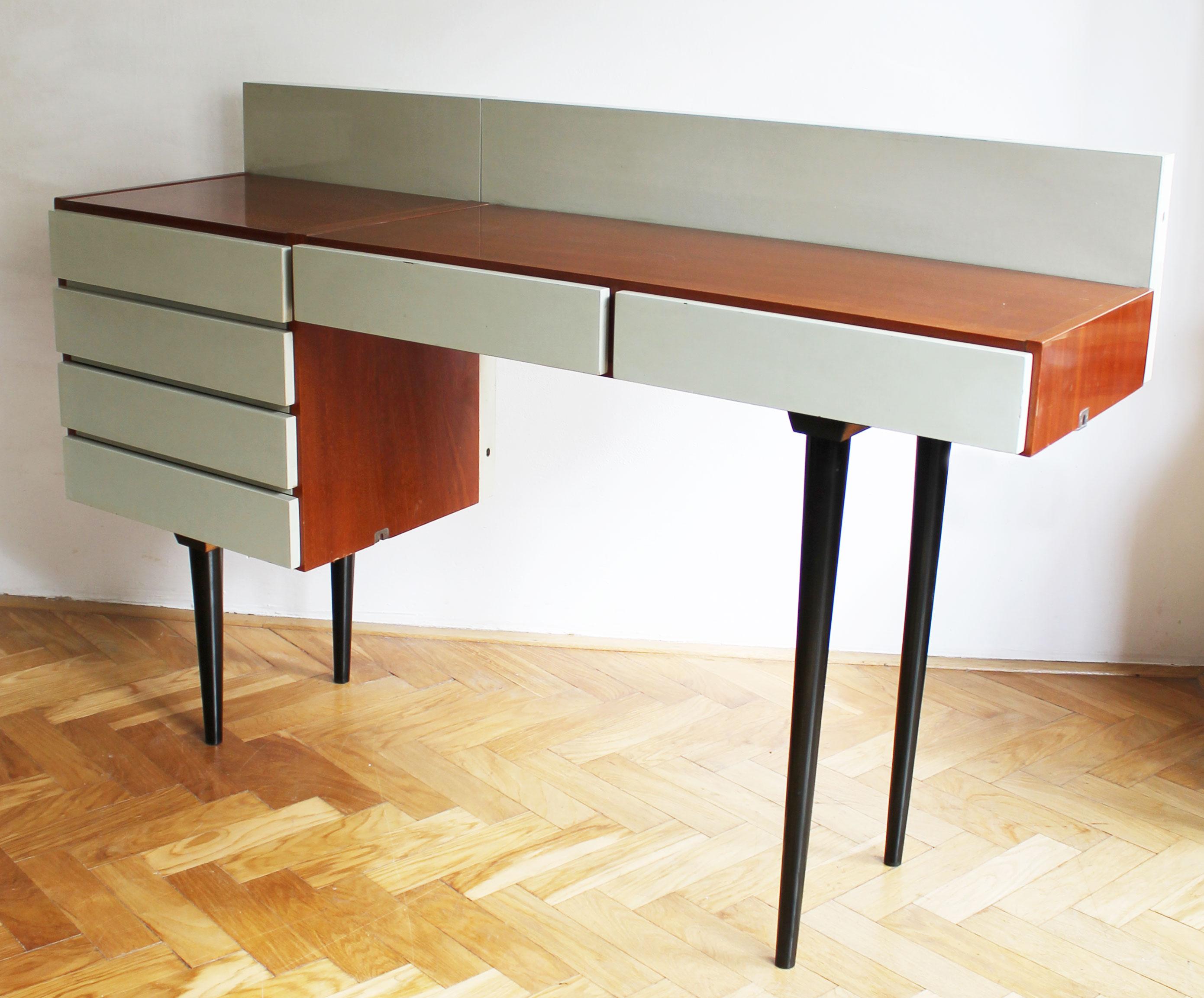 Dieser Schreibtisch war Teil eines modularen Wohnzimmersets und wurde in Collaboration von den Architekten Frantisek Mezulanik und Mojmir Pozar entworfen. Das Set wurde von UP Zavody in ihrem Werk in Bucovice bei Brünn hergestellt.

Dieser