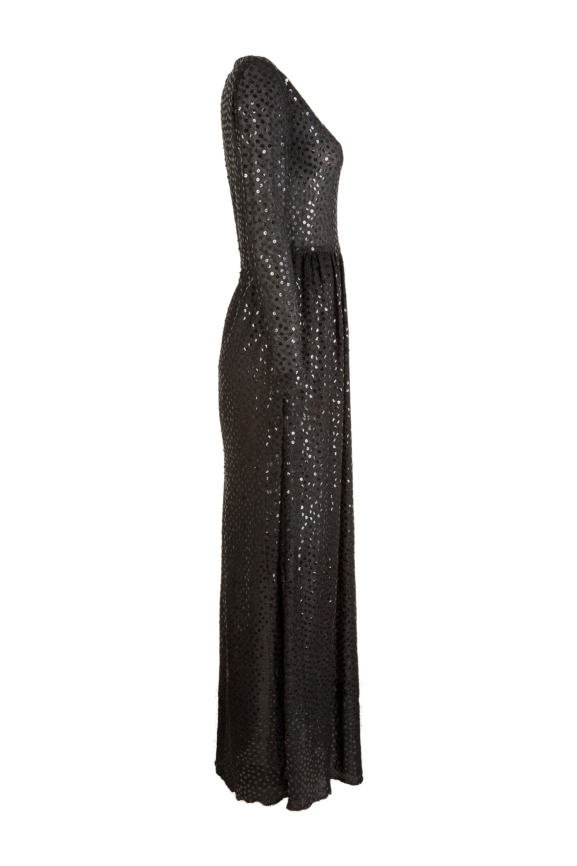 This sensational 1970s black sequinned evening gown is by Morty Sussman for Mollie Parnis Boutique and is in truly excellent vintage condition. The dress is elegant, with a modest V neckline, long sleeves and a full length skirt. The sheer black